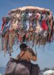 Strandverkäufer trägt einen mit bunten Bikinis behängten Schirm an einem überfüllten Mittelmeerstrand