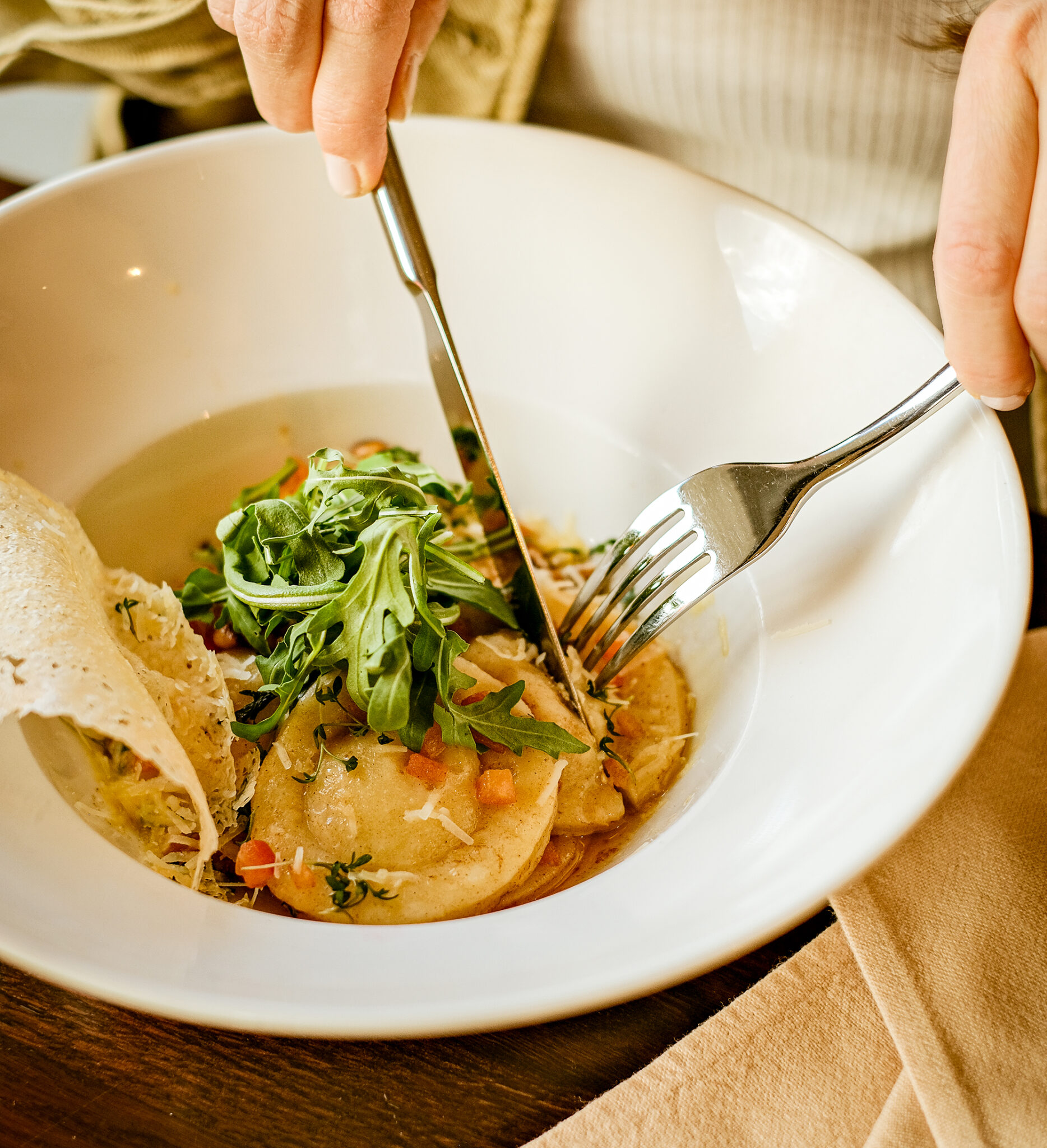Hände mit Besteck über einem weißen Teller mit Gnocchi, Rucola und Käsespänen