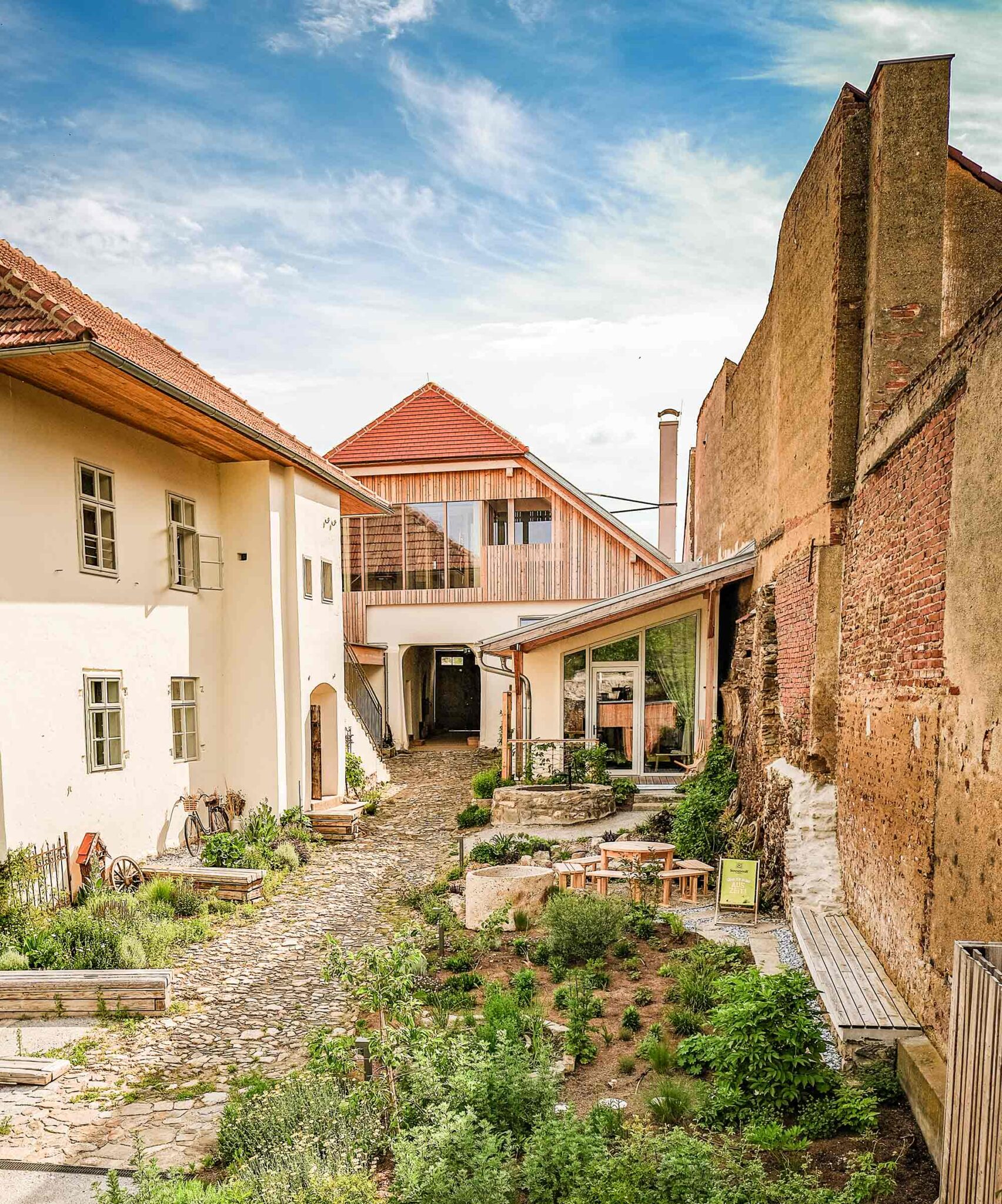 Begrünter Innenhof mit Natursteinpflaster, Kräuterpflanzen und renovierten Gebäuden