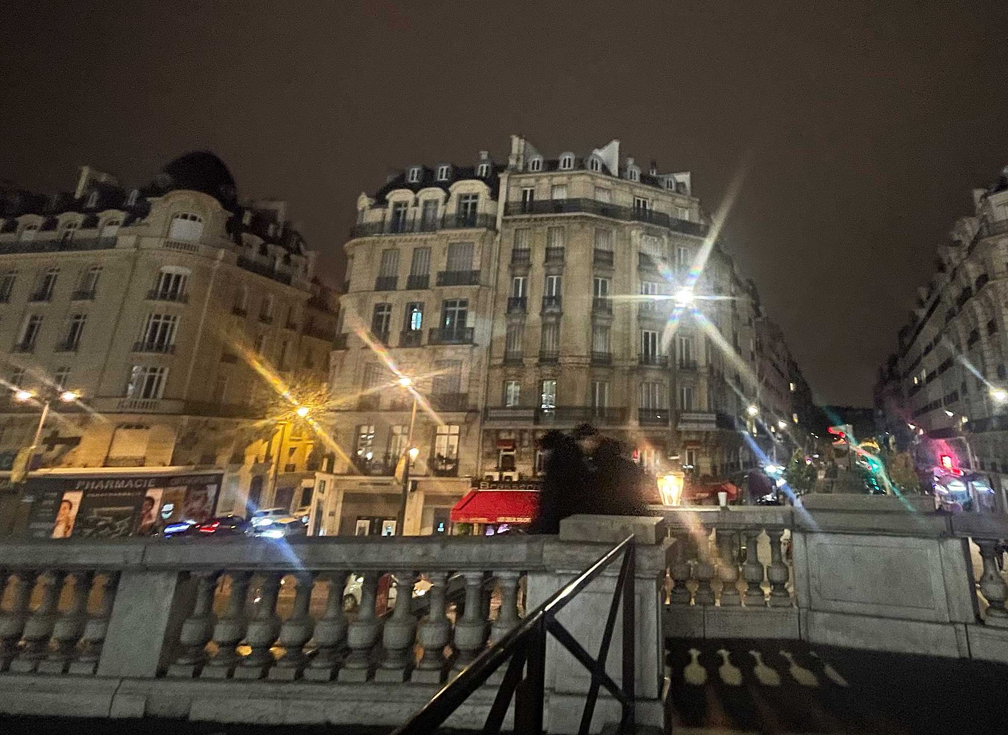 Nächtliches Paris mit beleuchteten Altbauten, einer Brasserie und funkendem Straßenlicht auf einer Brücke