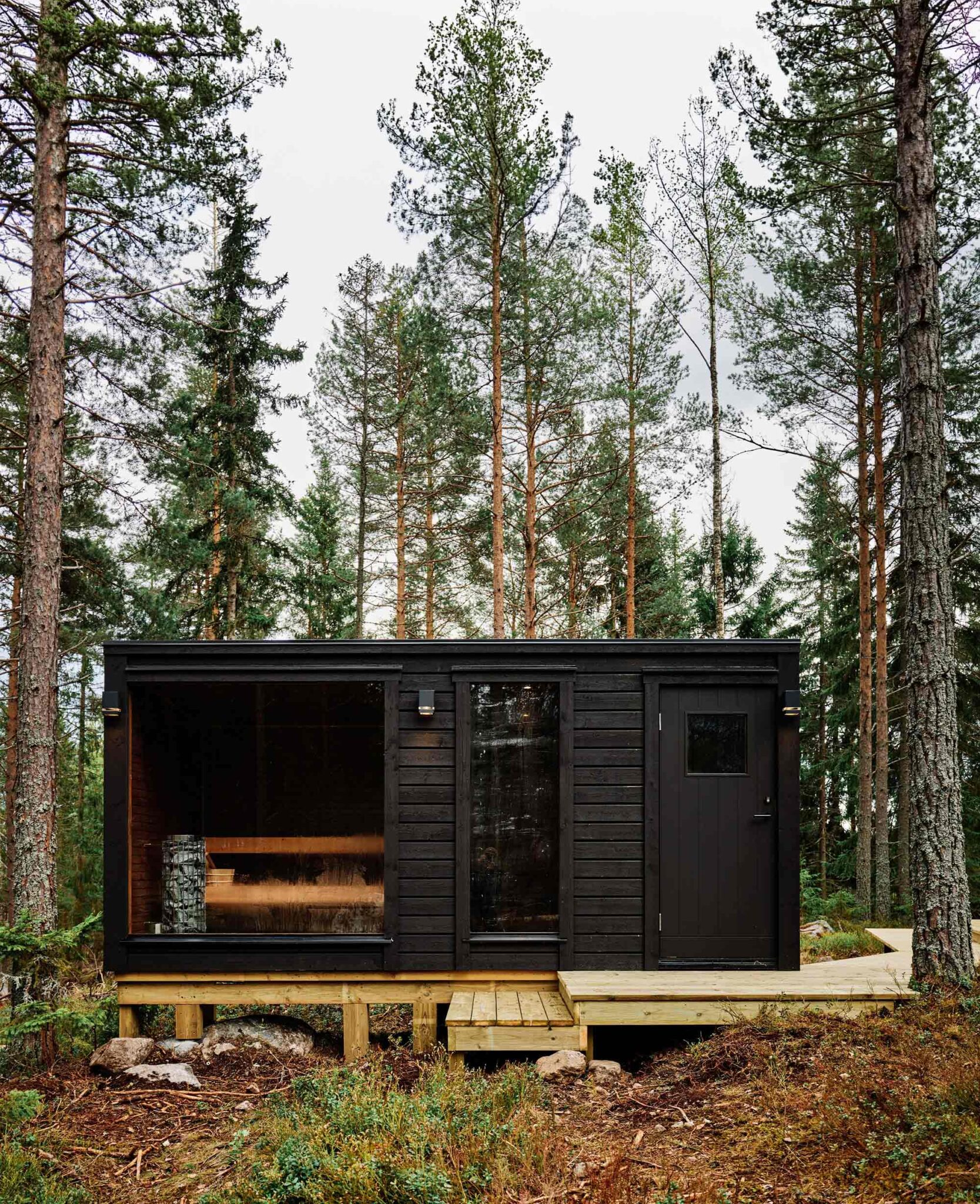 Schwarze Saunahütte auf Holzdeck inmitten eines schwedischen Kiefernwalds