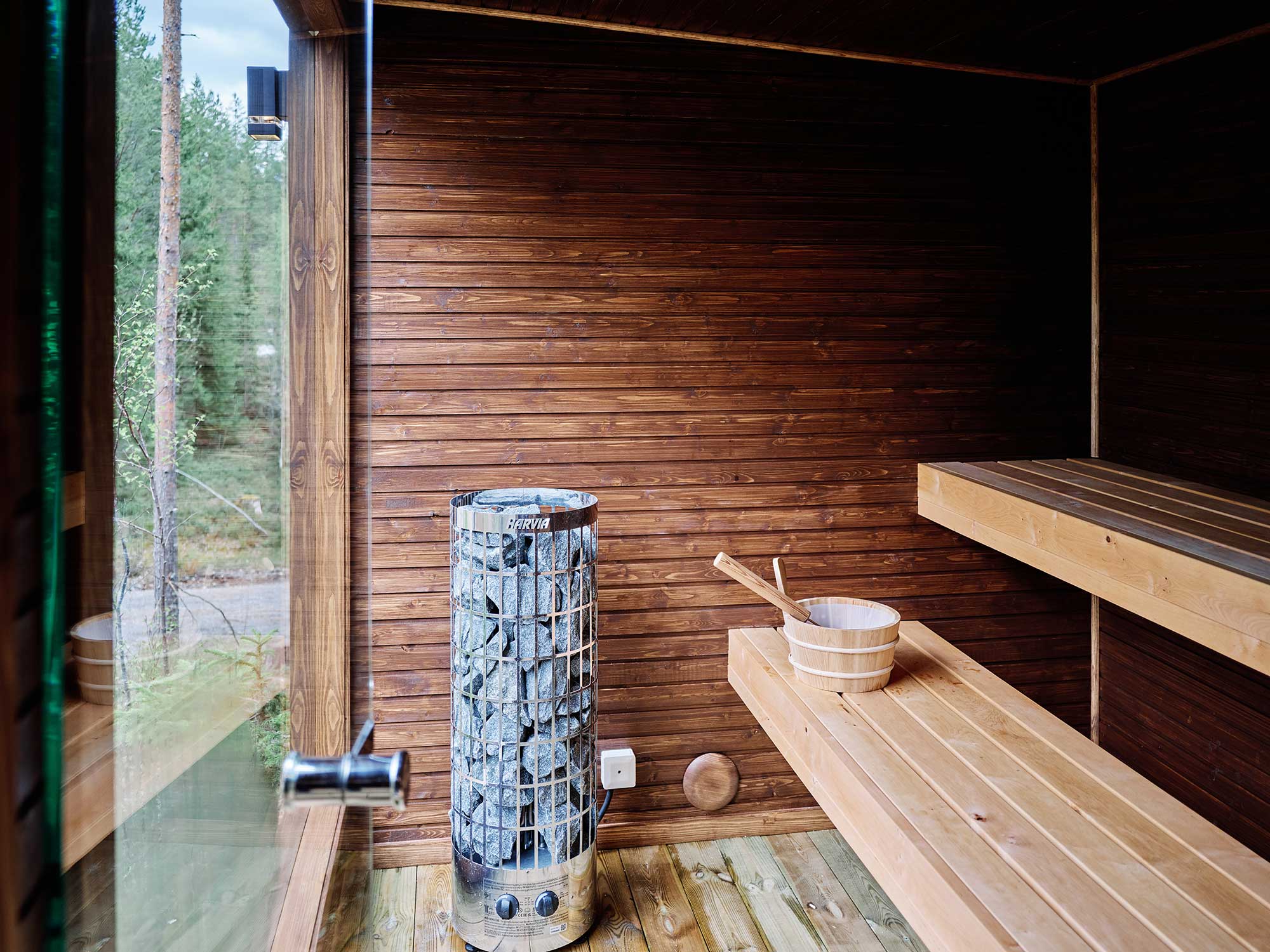 Innenansicht einer Holzsauna mit Harvia-Ofen, Holzeimern und Blick in den Wald