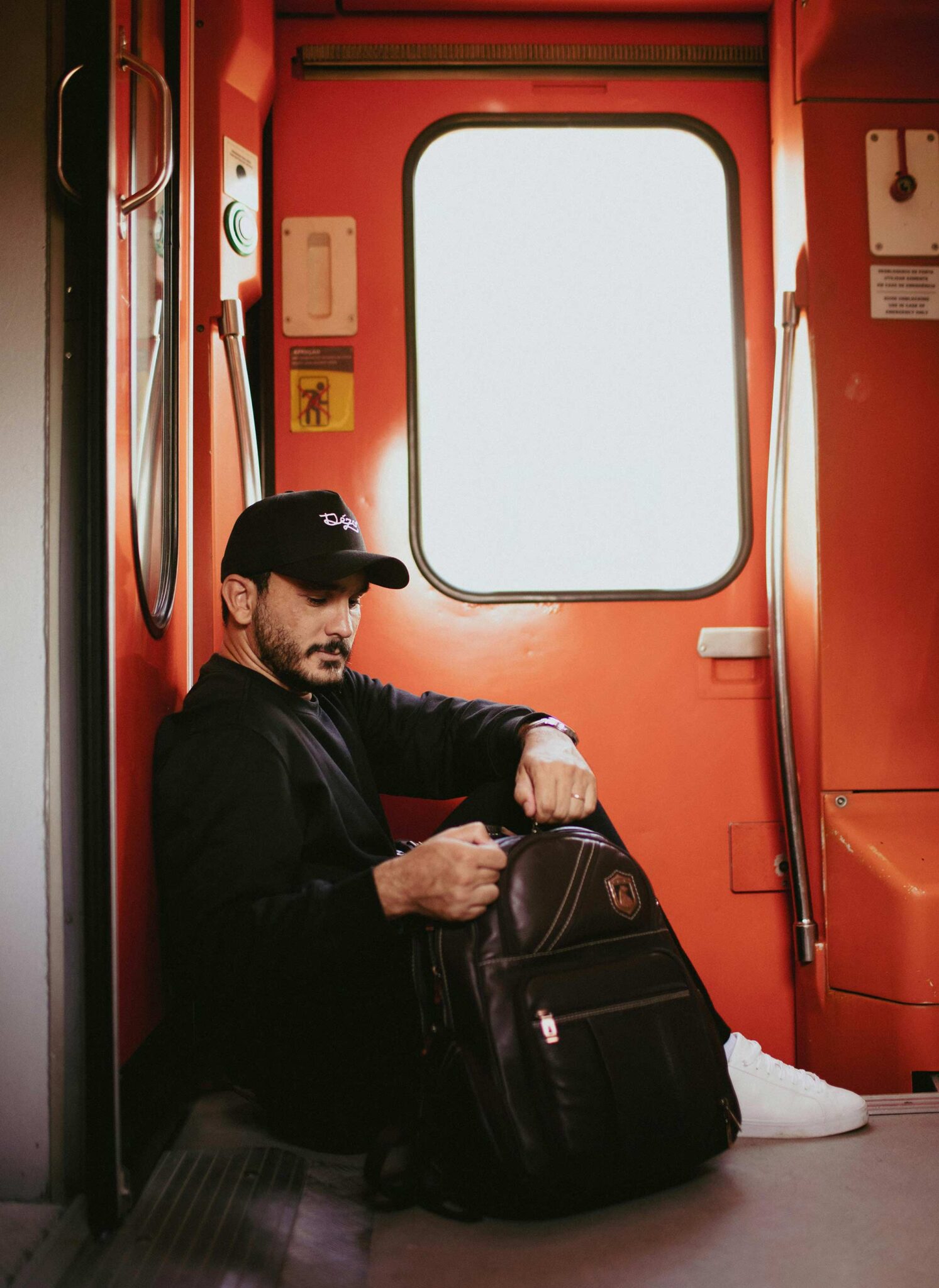Mann mit Cap sitzt mit Leder-Rucksack auf dem Boden eines Zugwaggons