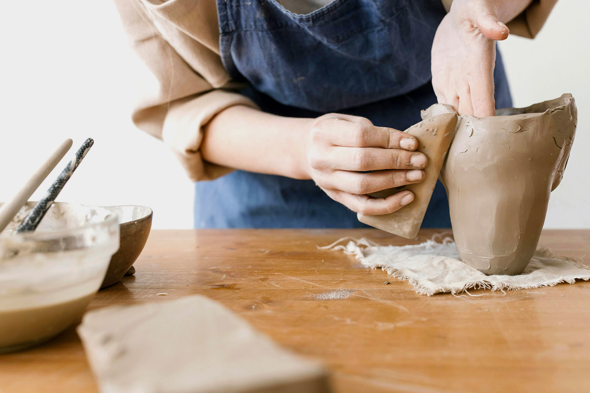Hände formen einen Tonbecher auf einem Holztisch beim Töpferkurs