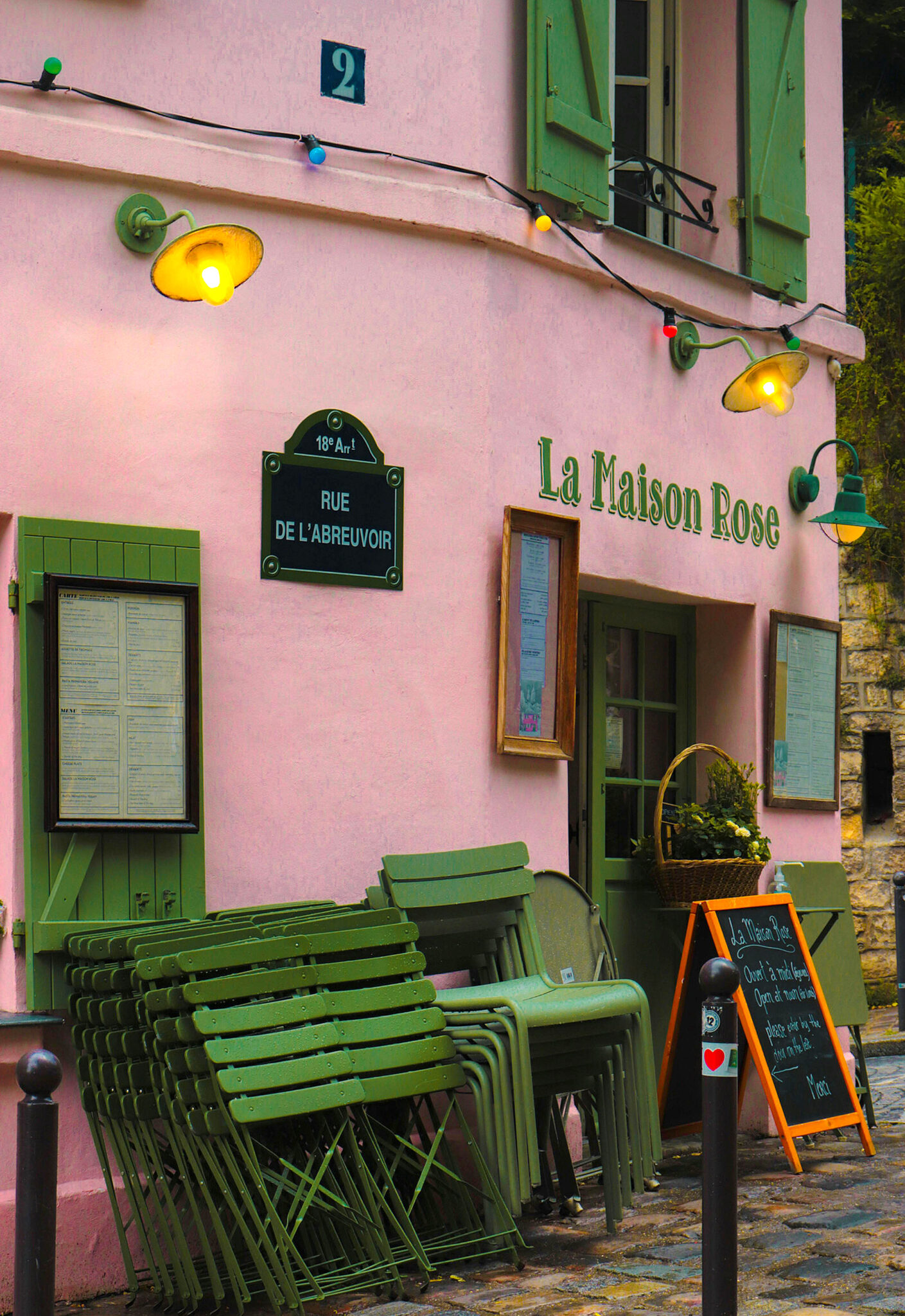 Rosa Fassade des Restaurants La Maison Rose in Montmartre mit grünen Stühlen und Lichterkette