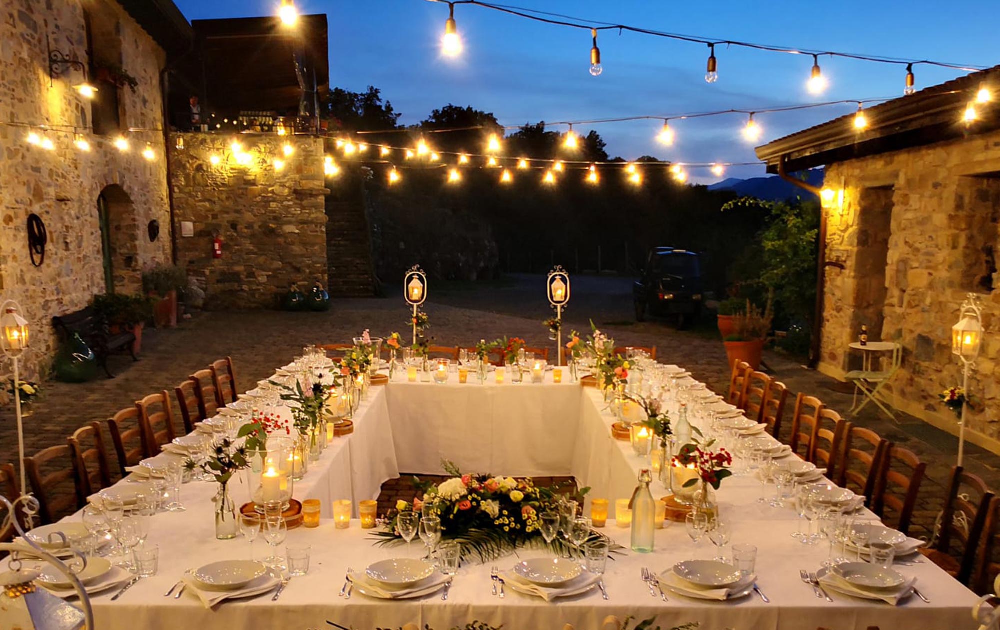 Festlich gedeckte Tafel unter Lichterketten im Innenhof eines toskanischen Steingehöfts bei Nacht