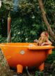 Frau entspannt in orangefarbener Outdoor-Badewanne umgeben von grünem Blattwerk