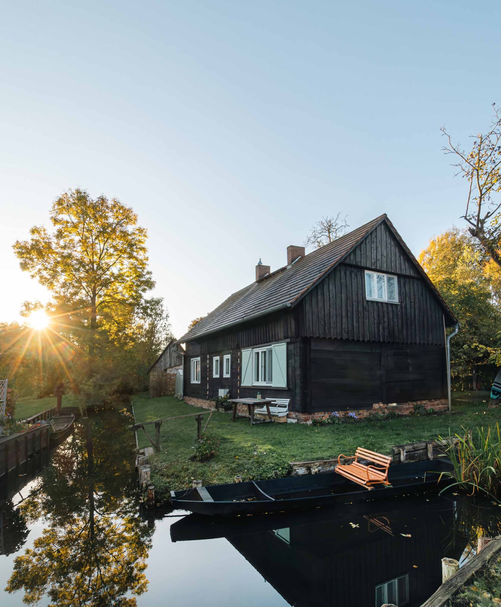 Holzhaus am Kanal im Spreewald bei Sonnenuntergang mit Boot im Vordergrund