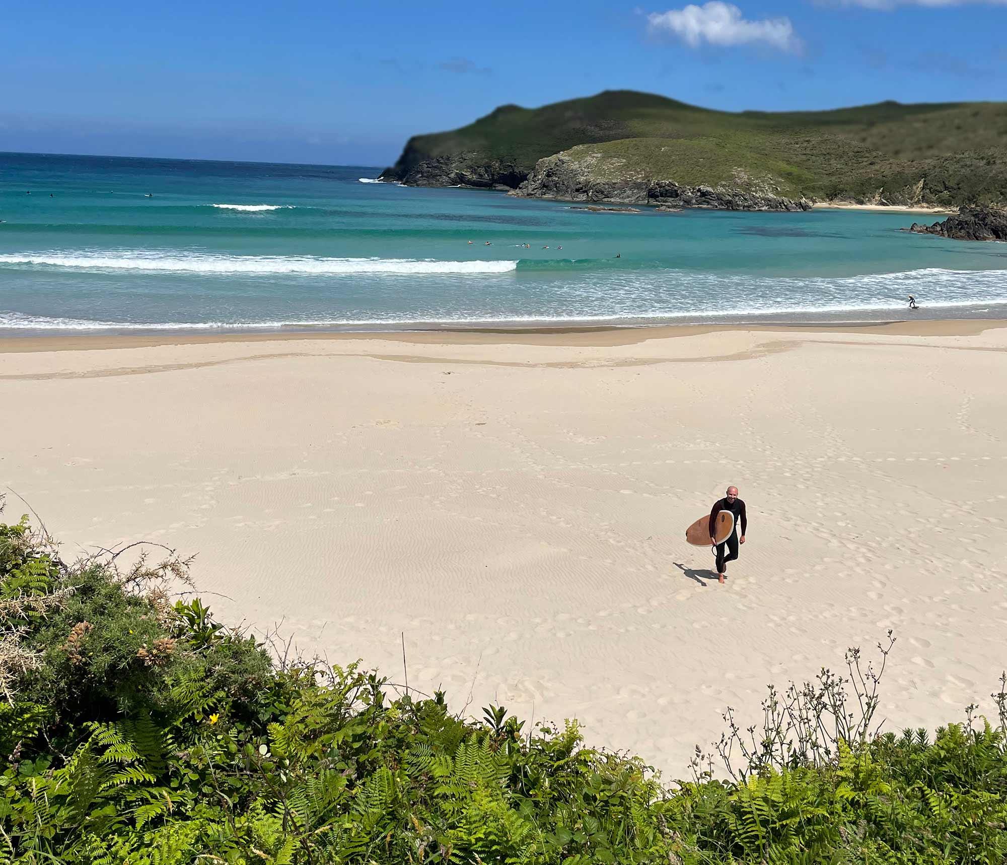 Surfer mit Board am weißen Sandstrand von Galizien mit türkisfarbenem Atlantik im Hintergrund