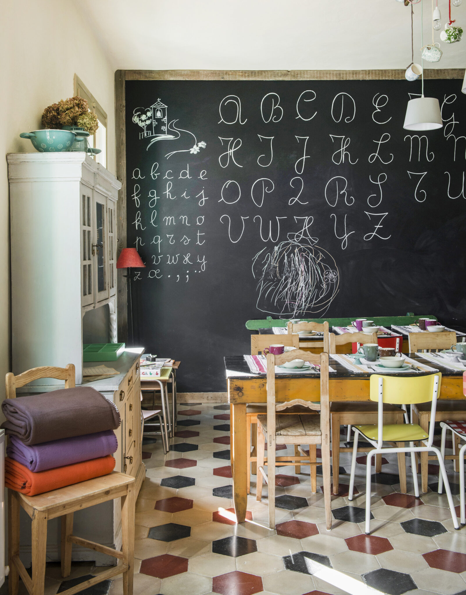 Gemütlicher Frühstücksraum im B&B La Scuola mit Tafelwand voller Schreibschrift-Alphabet, bunten Hexagon-Fliesen und Vintage-Holzmöbeln