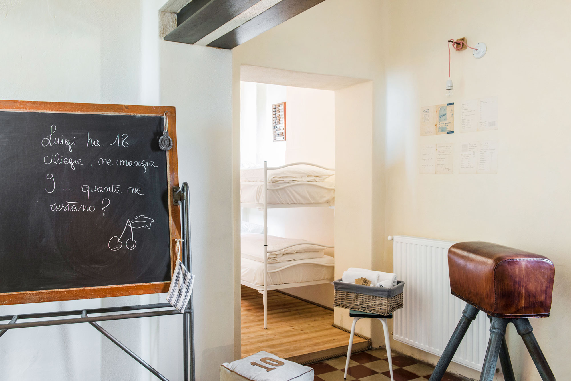 Alte Schultafel mit handgeschriebener Rechenaufgabe auf Italienisch, Blick in ein gemütliches Zimmer mit weißem Etagenbett