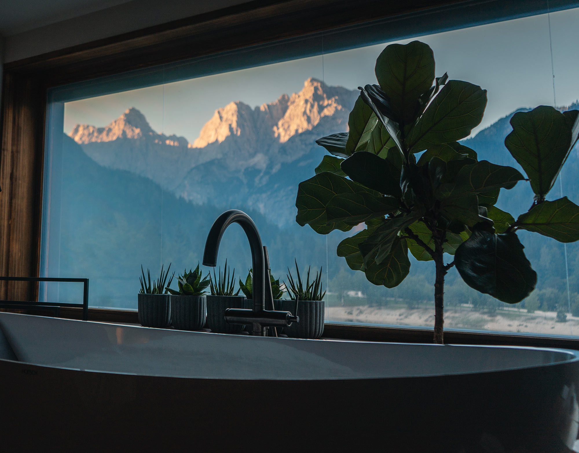 Freistehende Badewanne im Zimmer des Boutique Hotels Milka in Kranjska Gora mit großem Panoramafenster und Blick auf die im Abendlicht leuchtenden Julischen Alpen