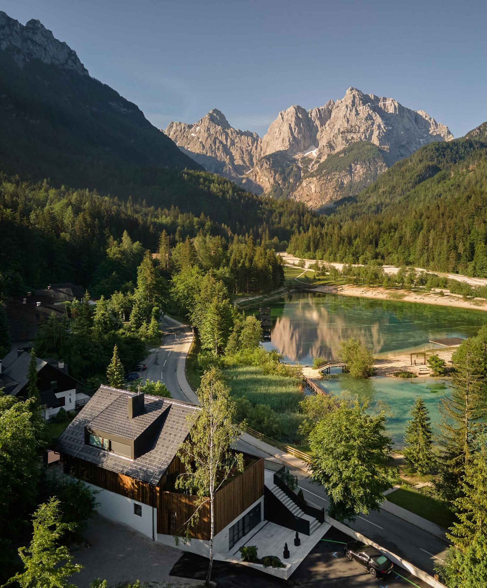 Luftaufnahme des Boutique Hotels Milka in Kranjska Gora: Hotelgebäude mit Holzfassade direkt am türkisfarbenen Jasna-See mit Blick auf die Julischen Alpen
