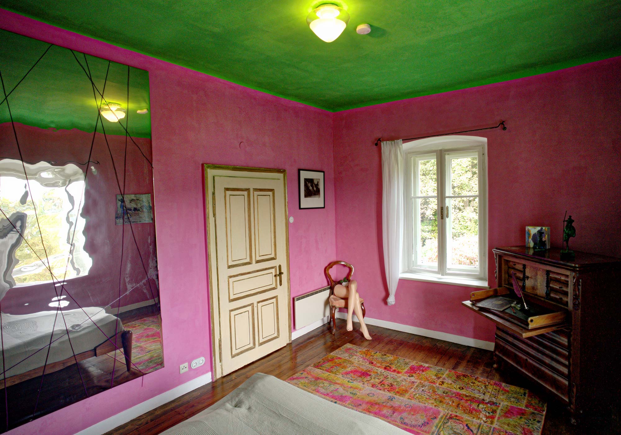 Farbenfrohes Schlafzimmer mit pinken Wänden, grüner Decke, antikem Sekretär und großem Spiegel im Ferienhaus rosa und blau am See