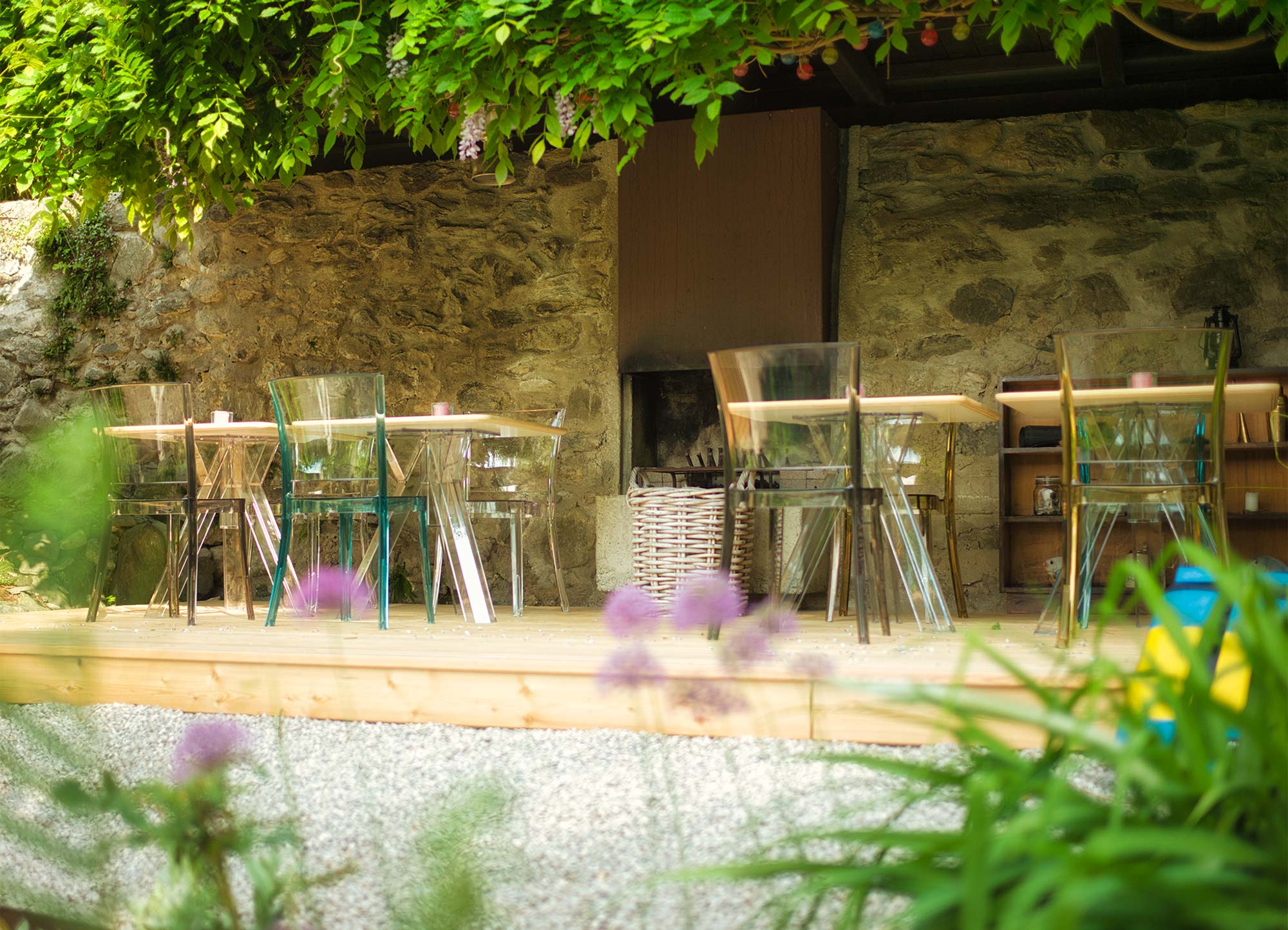 Gemütlicher Sitzbereich mit transparenten Designer-Stühlen, Holzdeck und offenem Kamin unter einer begrünten Pergola im Garten