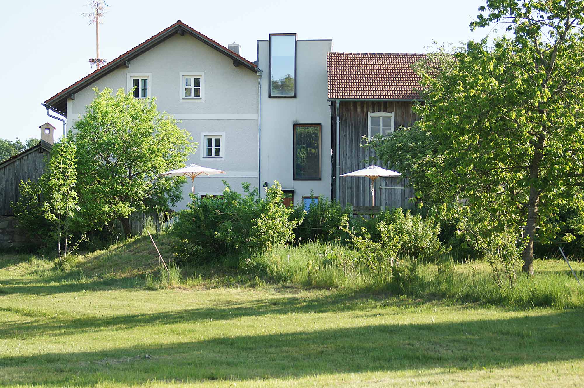 Außenansicht des kernsanierten Vierseitenhofs Moosham13 in Grafenau mit Altbau, modernem Glasanbau und Garten