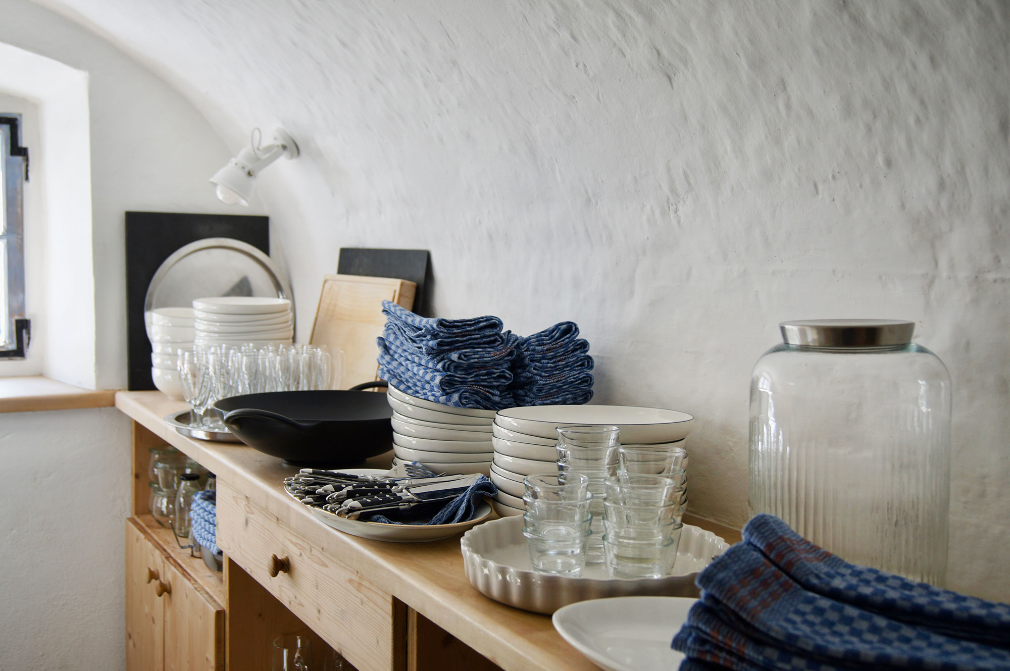 Holzanrichte mit weißem Geschirr, blauen Leinenservietten und Gläsern vor Naturkalkwand in der Ferienwohnung Moosham13