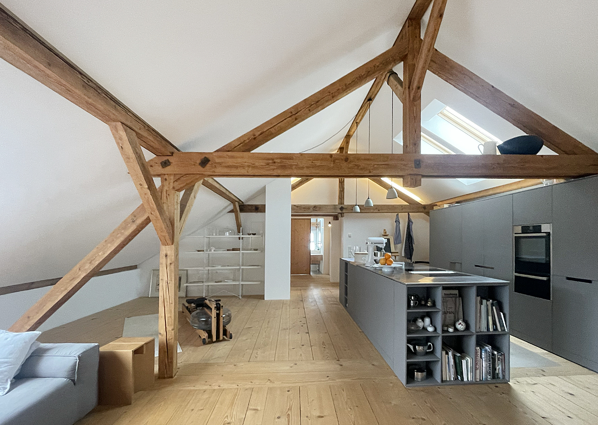 Offenes Loft im ehemaligen Heustadel von Moosham13 mit freiliegenden Holzbalken, grauer Designküche und Holzdielen aus dem eigenen Wald
