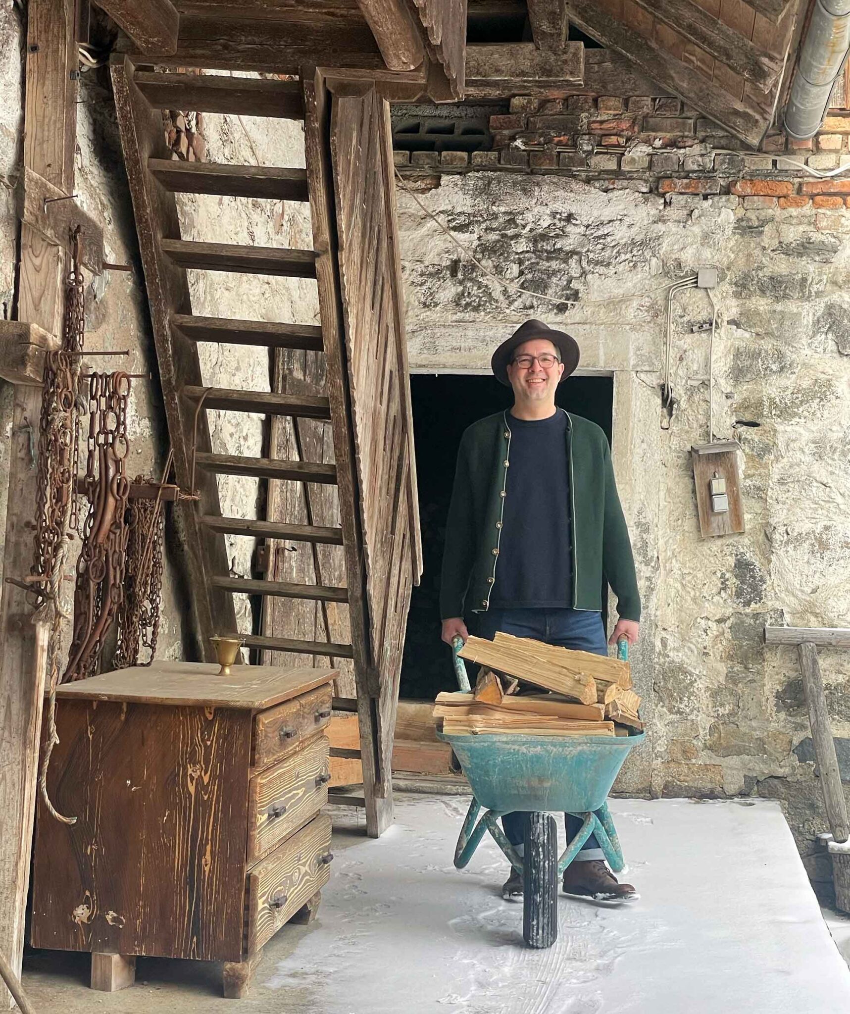 Gastgeber Reinhold Windorfer-Bogner mit Schubkarre voller Feuerholz im historischen Innenhof des Moosham13