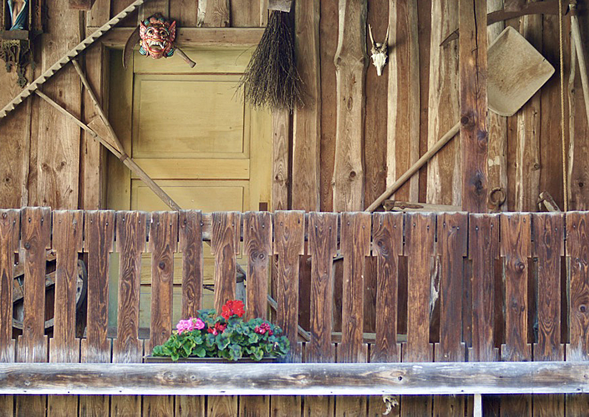 Alter Holzbalkon der Scheune in der Ferienwohnung Moosham13 in Grafenau mit Kranz-Maske, Tierschädel und Geranien