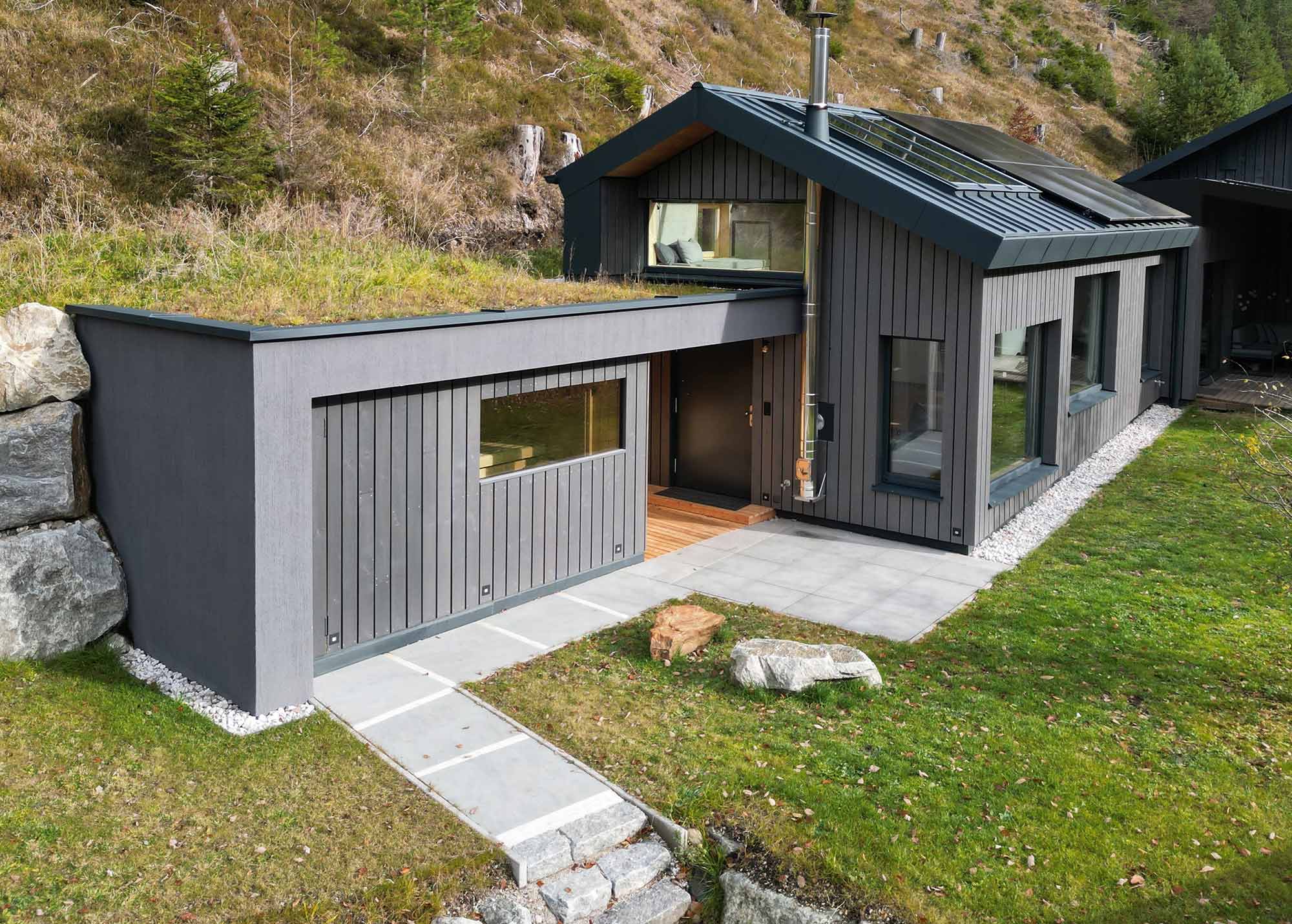 Außenansicht des Flussbett Hotels in Tirol: modernes Holzgebäude mit dunkler Fassade, Gründach und großen Fensterfronten, eingebettet in die Berglandschaft