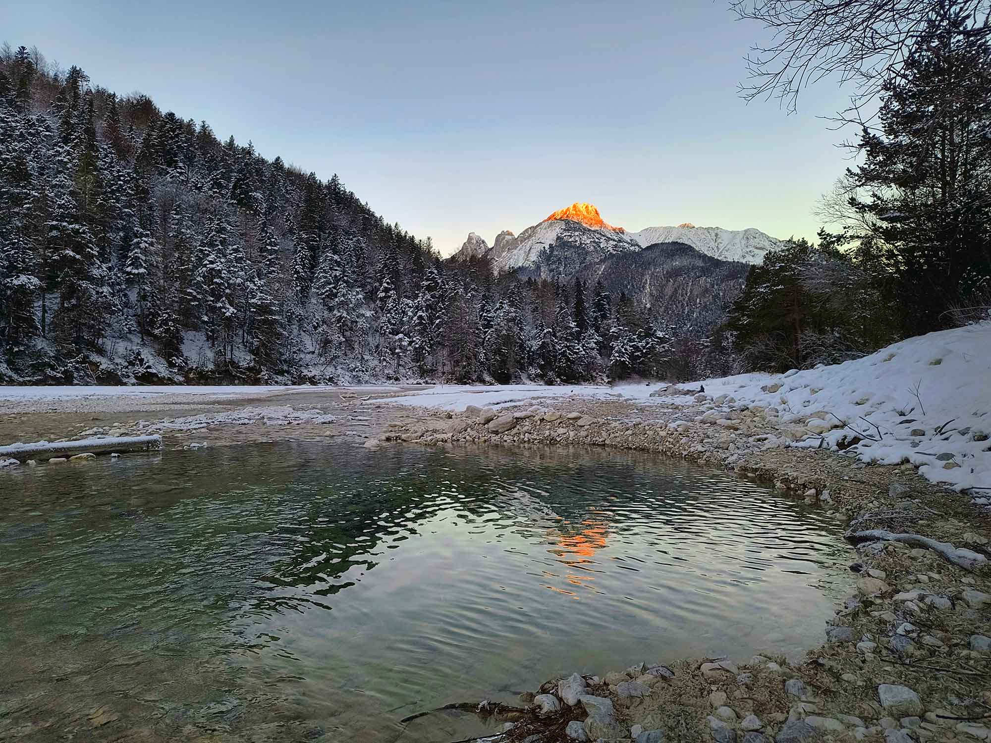 Türkisfarbene Isar im Winter beim Flussbett Ferienunterkunft in Tirol, umgeben von schneebedeckten Wäldern und Bergen im Abendlicht