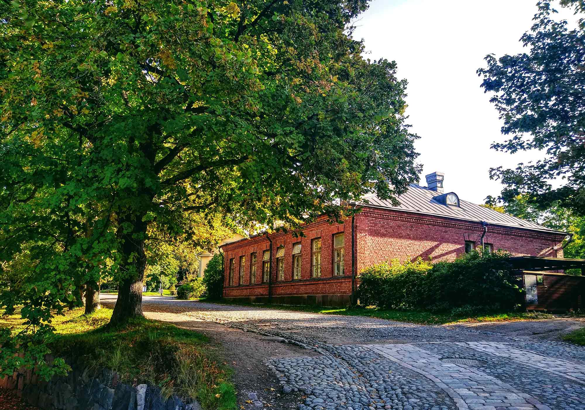 Historisches rotes Backsteingebäude des Hostel Suomenlinna umgeben von grünen Bäumen auf der UNESCO-Weltkulturerbe-Festungsinsel