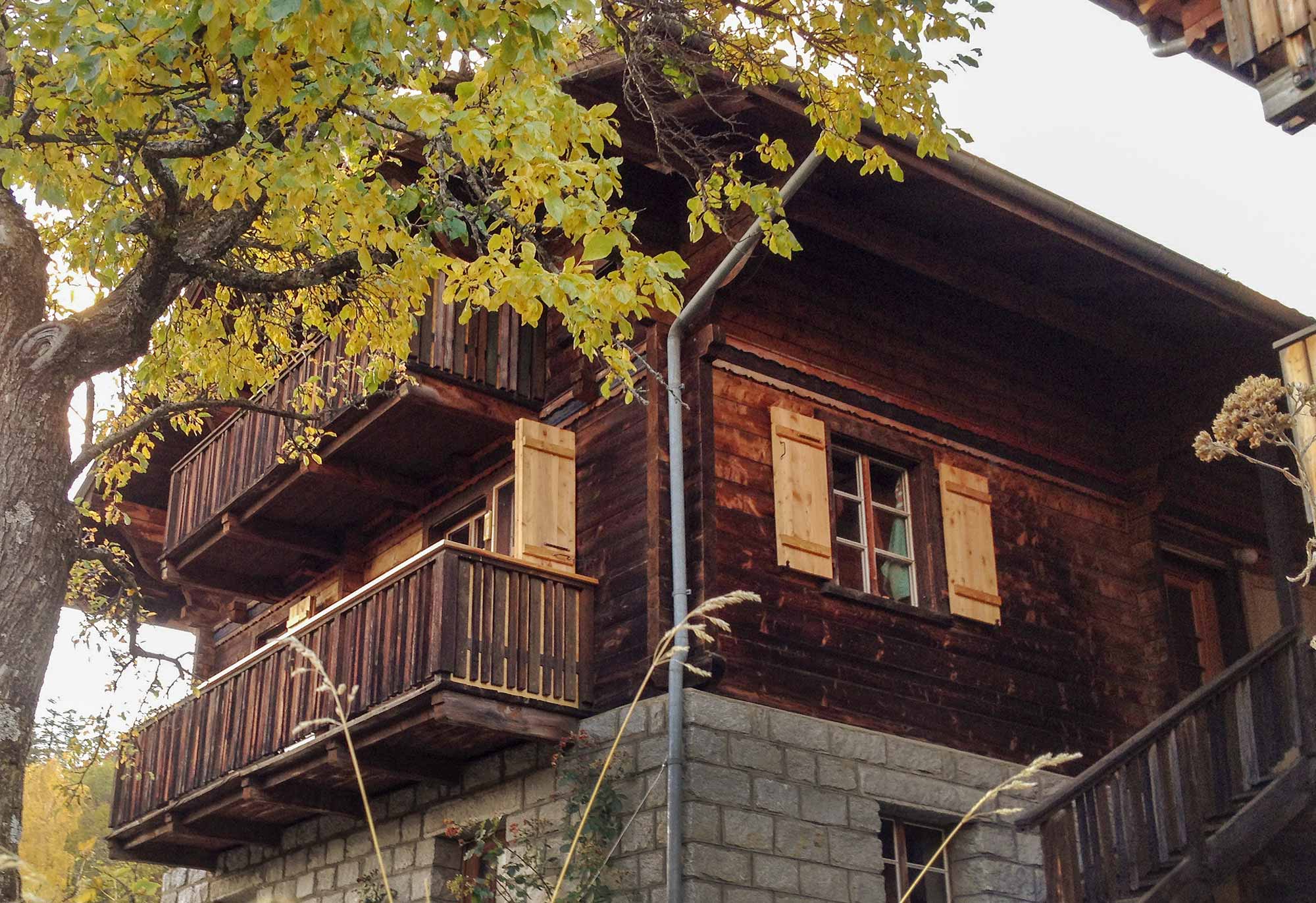 Außenansicht des Josihauses in Martisberg im Wallis: traditionelles Walliser Holzhaus mit dunkler Holzfassade, zwei Balkonen und Holzläden im Herbst