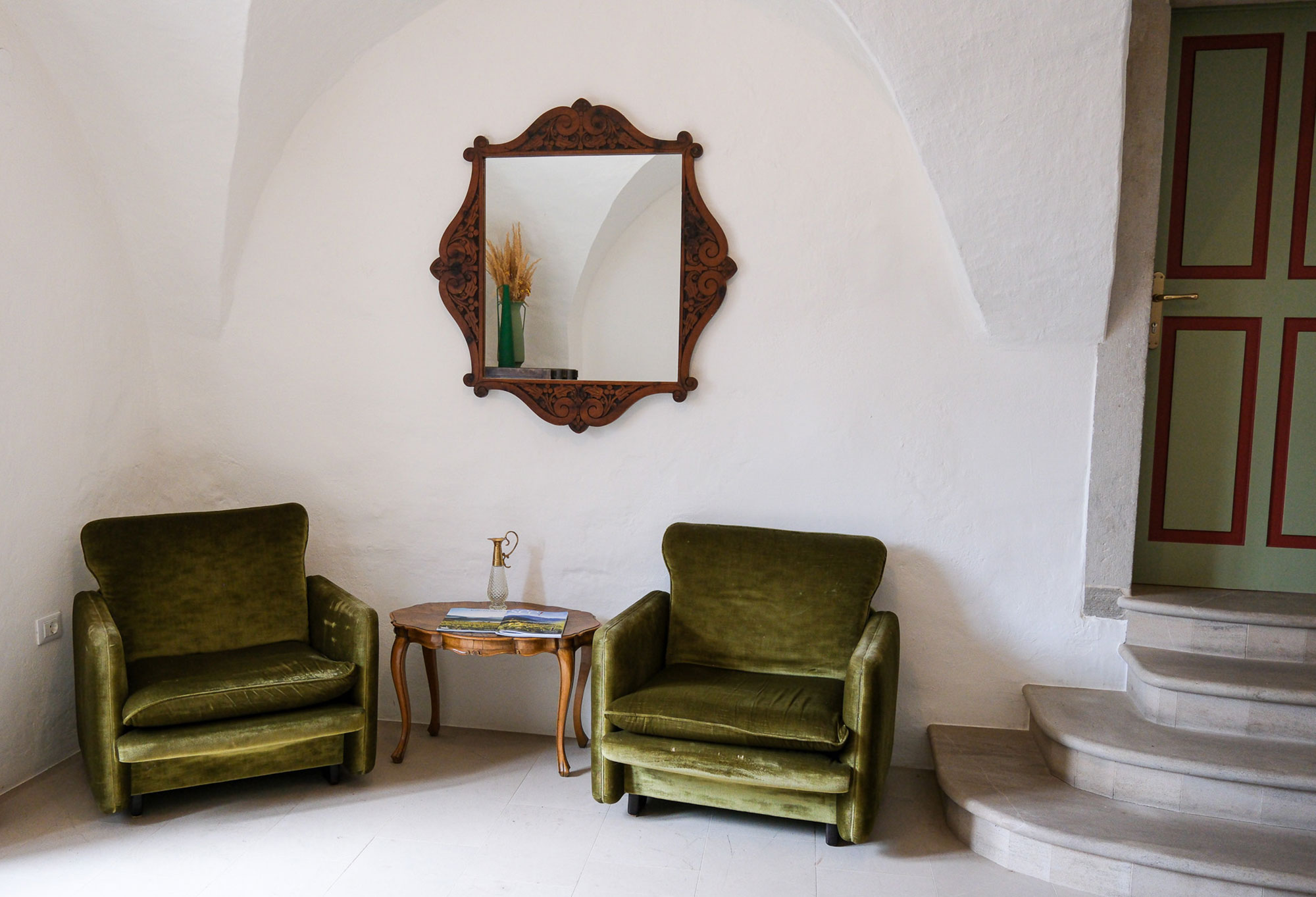 Eingangsbereich der Pension Leuchtenburg in Kaltern mit zwei grünen Samtsesseln, antikem Holzspiegel und historischem Gewölbe