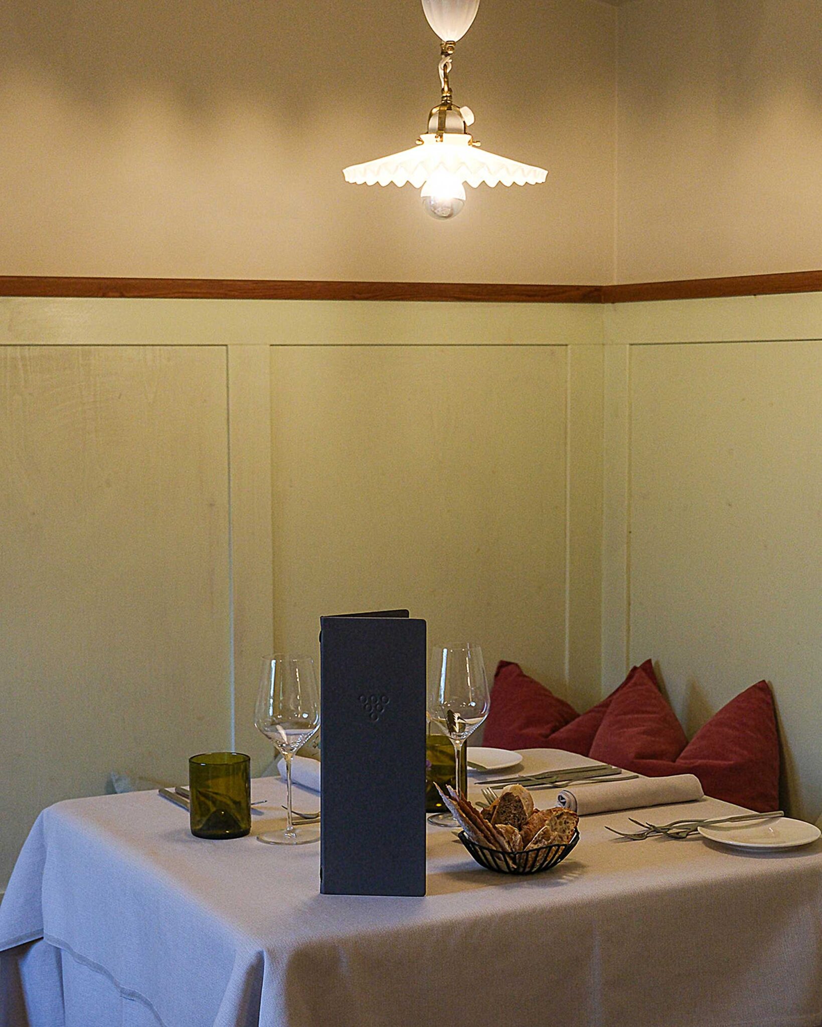 Gedeckter Tisch im Restaurantgewölbe des Stroblhof Eppan mit Weingläsern, Brotkorb, roter Kissenbank und gedimmter Hängelampe