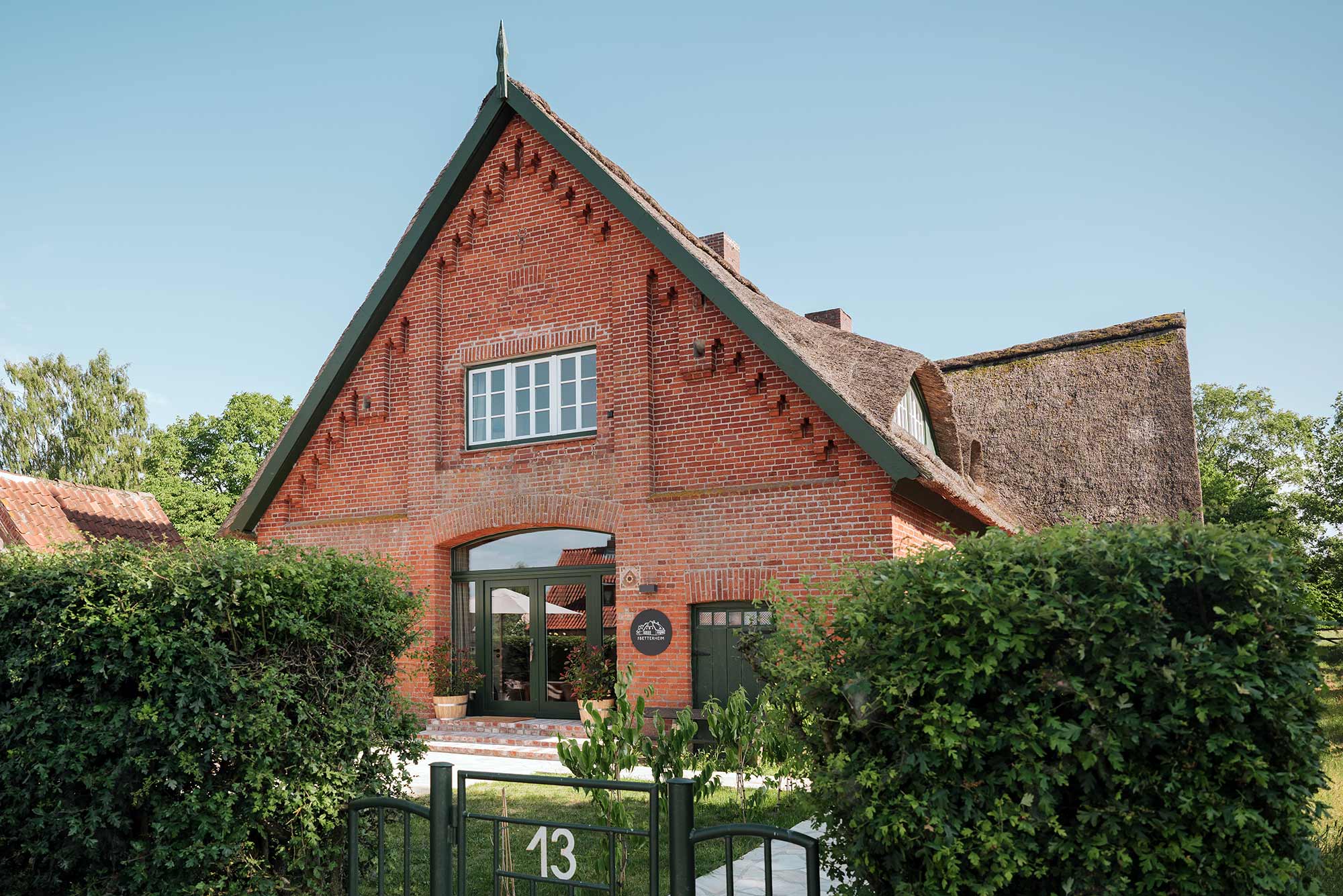 Giebelfassade der ehemaligen Schule THE BETTERHEIM mit rotem Backstein, Reetdach und grünem Eingangsbereich in Kittlitz