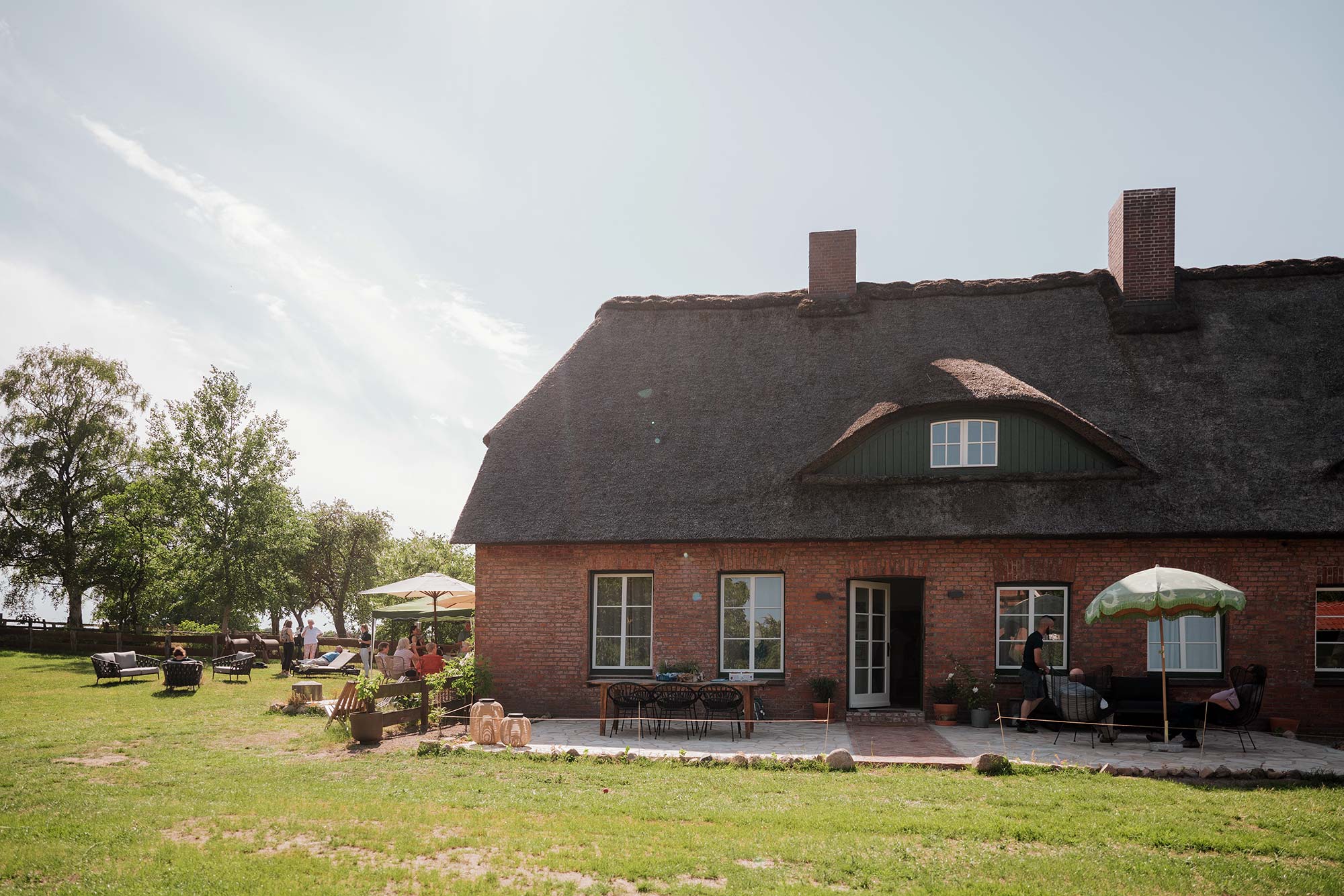 Reetgedecktes Backsteinhaus THE BETTERHEIM mit sonniger Terrasse, Sitzgruppen und Gästen im Garten in Kittlitz