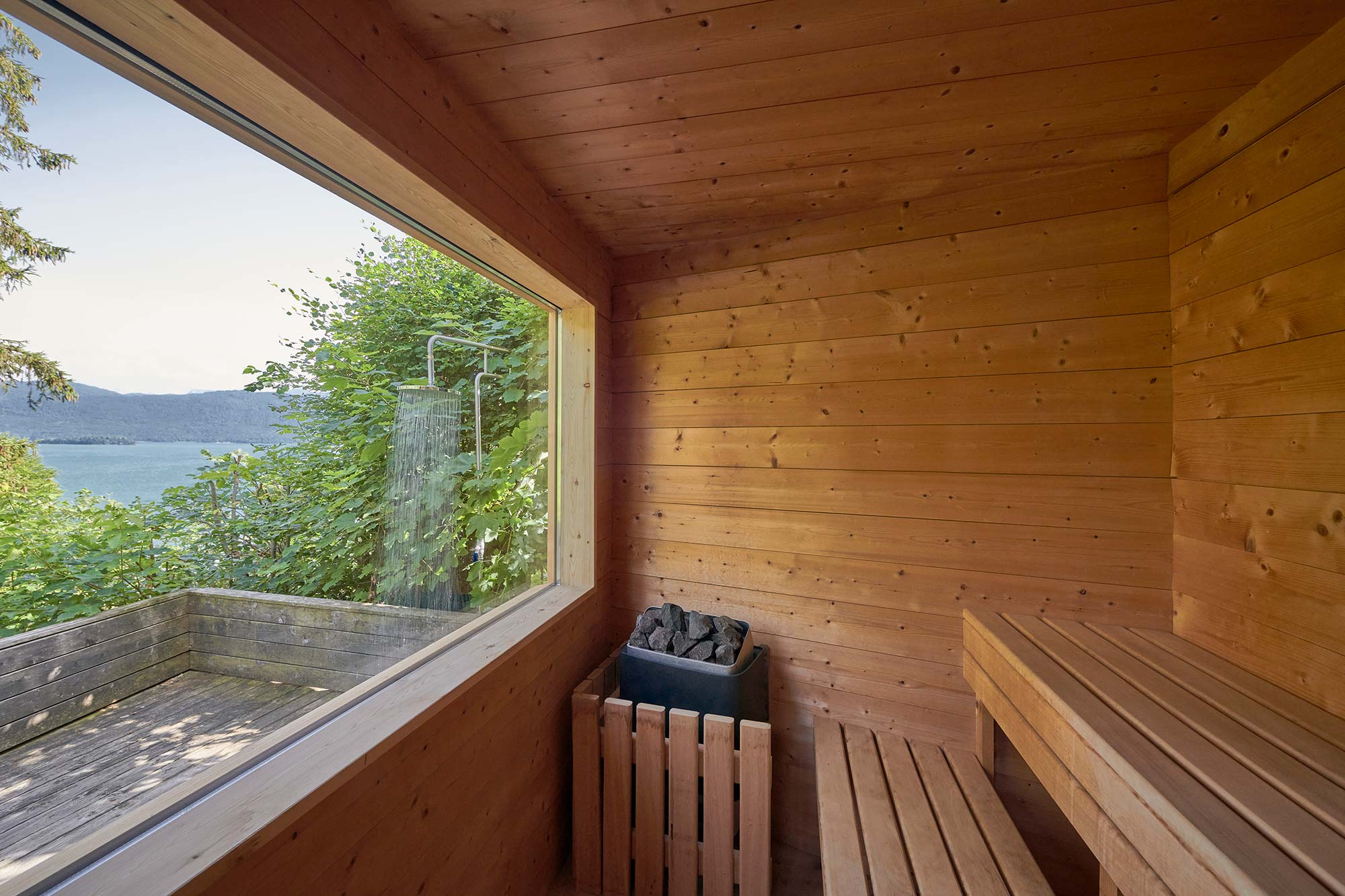 Innenraum der Panoramasauna im Ferienhaus Urfeld 26 mit großem Glasfenster, Blick auf Walchensee und Berge, Saunaofen und Holzliegeflächen