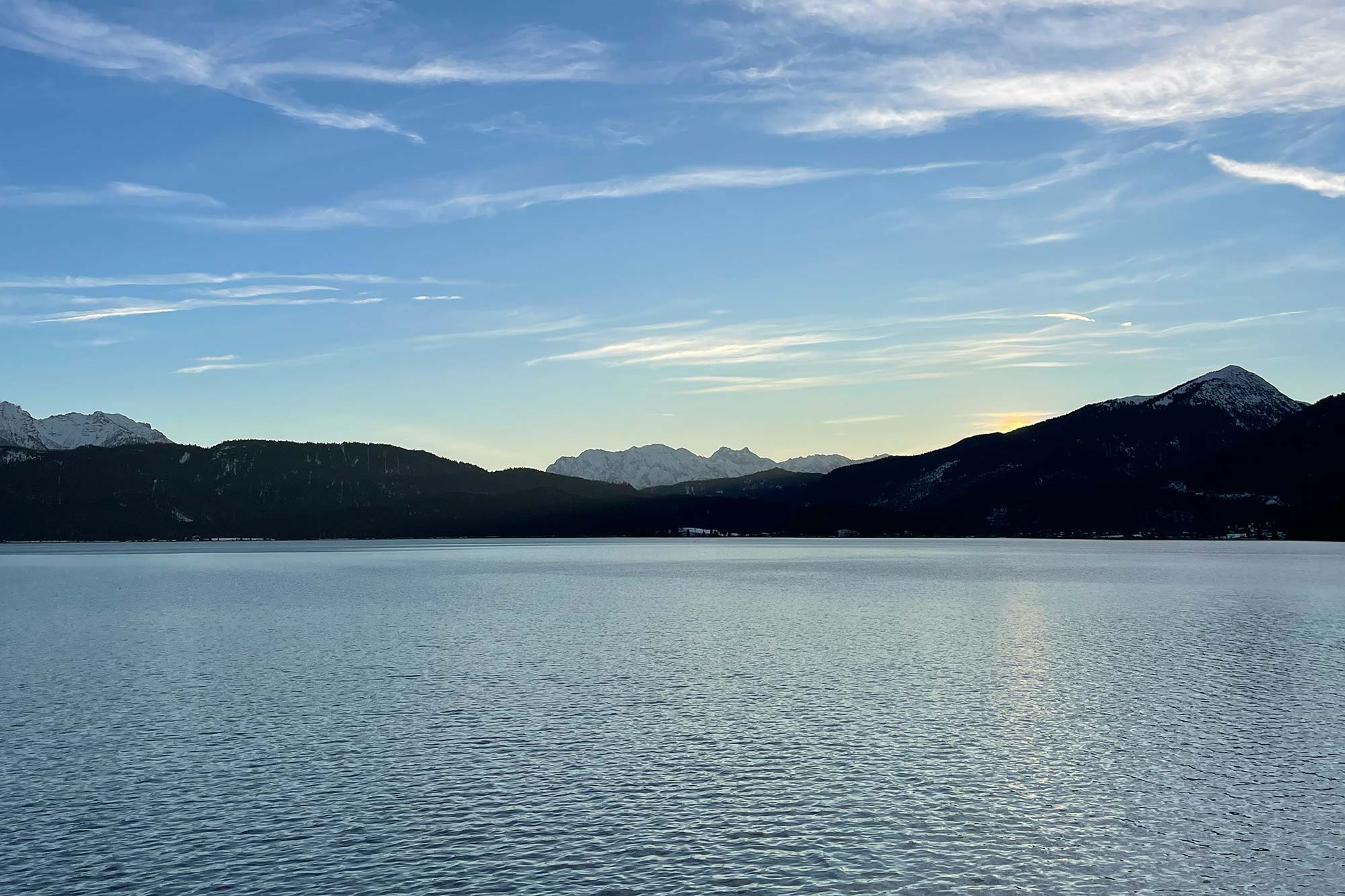 Winterliches Panorama des Walchensees in Bayern im Abendlicht mit schneebedeckten Bergkuppen und weitem Himmel