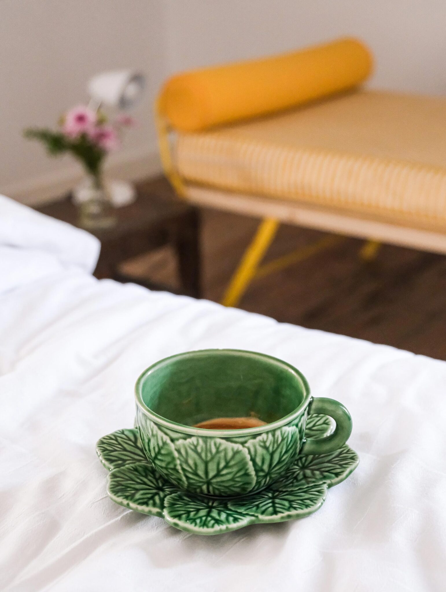 Grüne Vintage-Kaffeetasse auf dem Bett neben gelber Bank im Baixa House, Lissabon