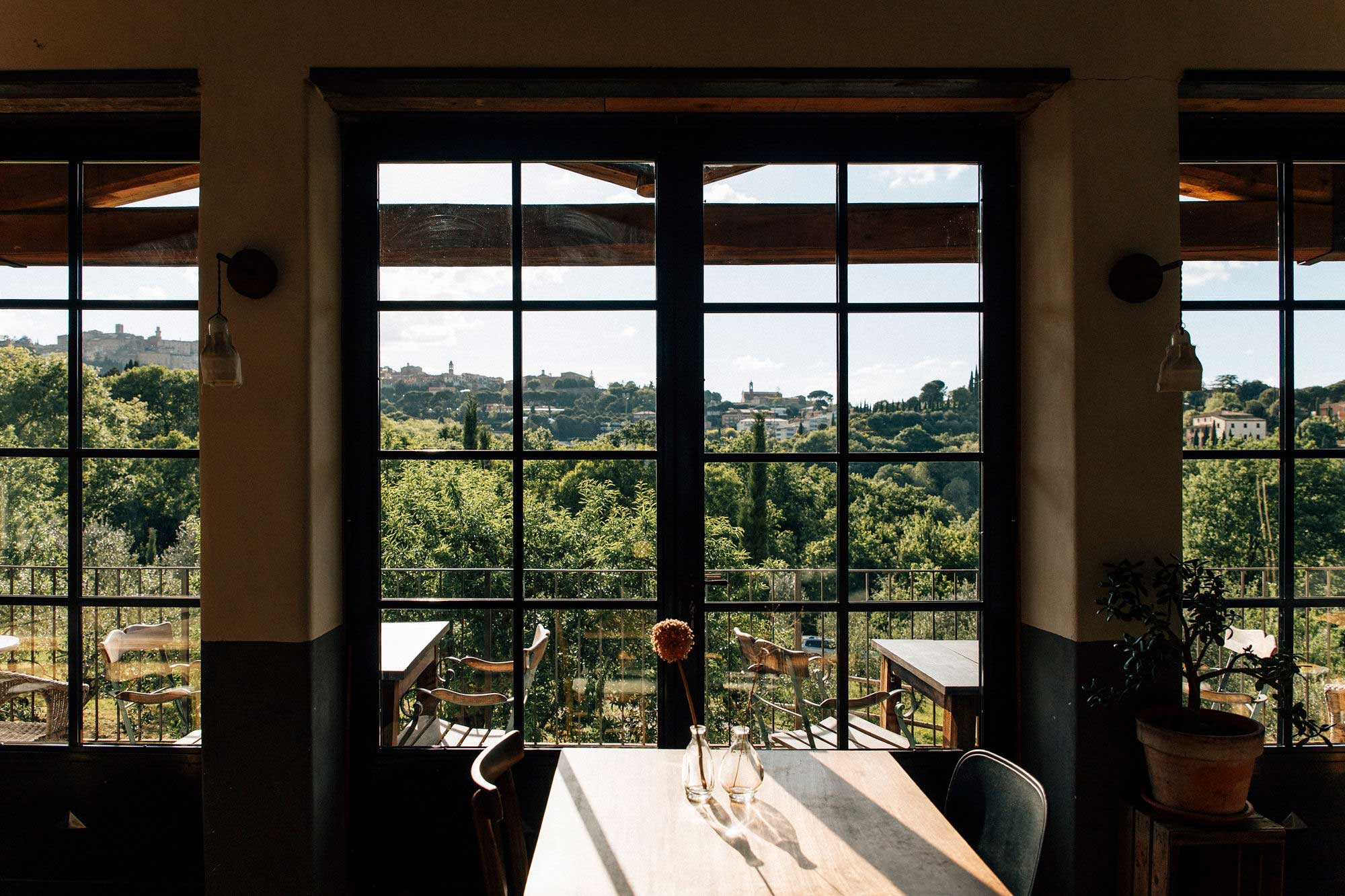 Blick durch große Sprossenfenster auf die toskanische Hügellandschaft mit Olivenbäumen und der Altstadt von Montepulciano