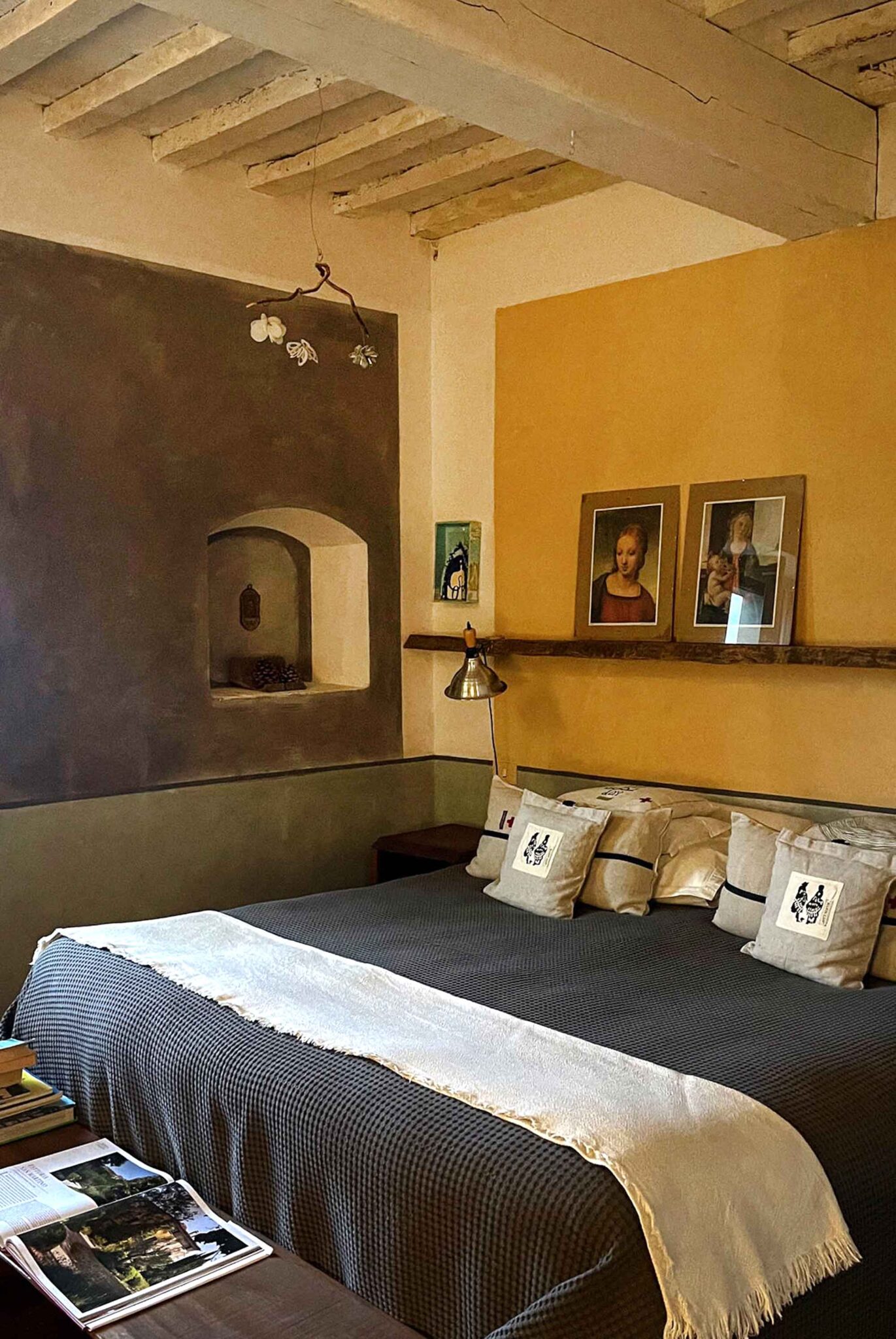 Gemütliches Schlafzimmer mit gewölbter Holzdecke, ockergelber Wand und gerahmten Kunstdrucken in der Fattoria San Martino