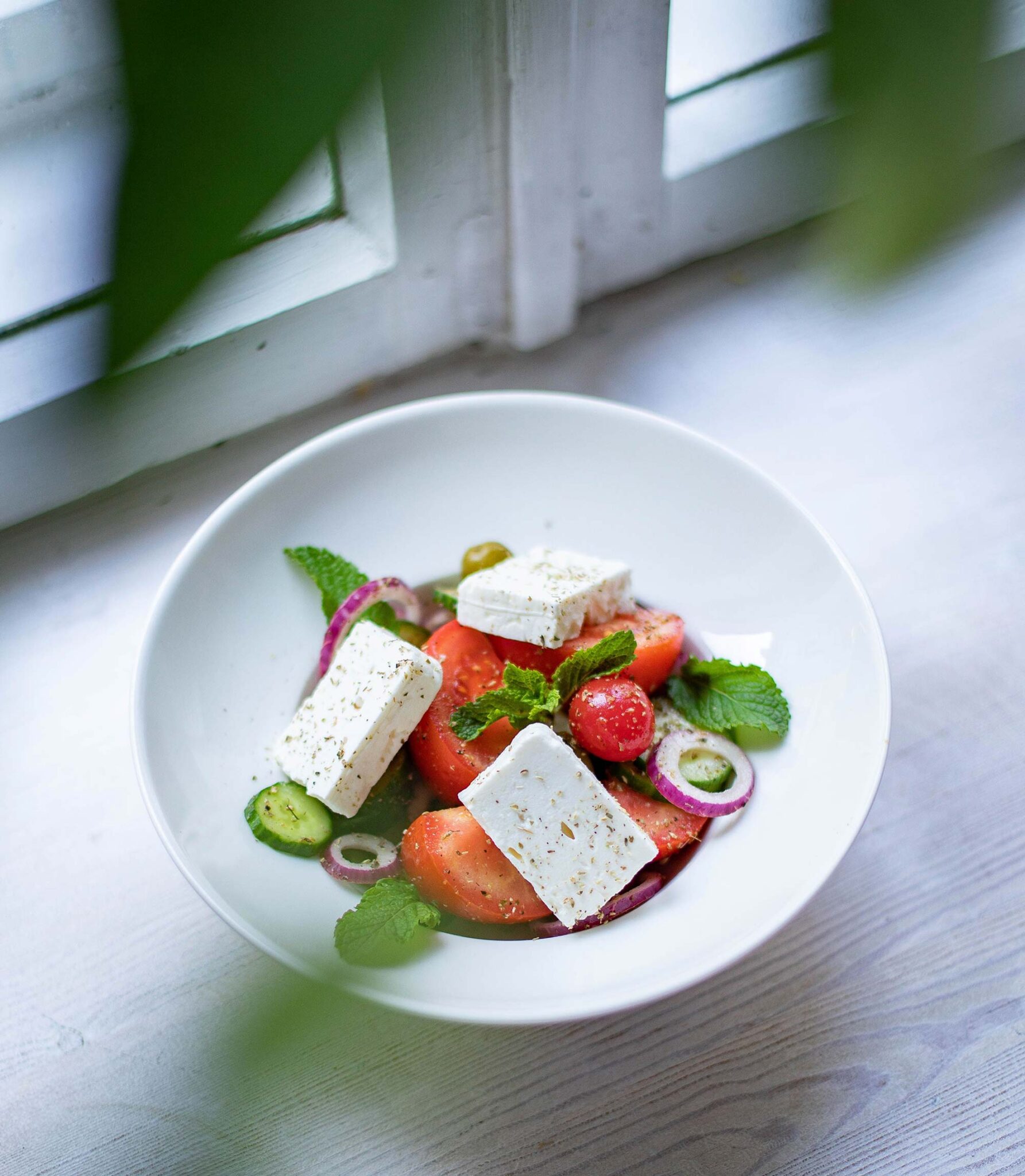 Griechischer Bauernsalat mit Tomaten, Feta, roten Zwiebeln und frischer Minze am Fenster