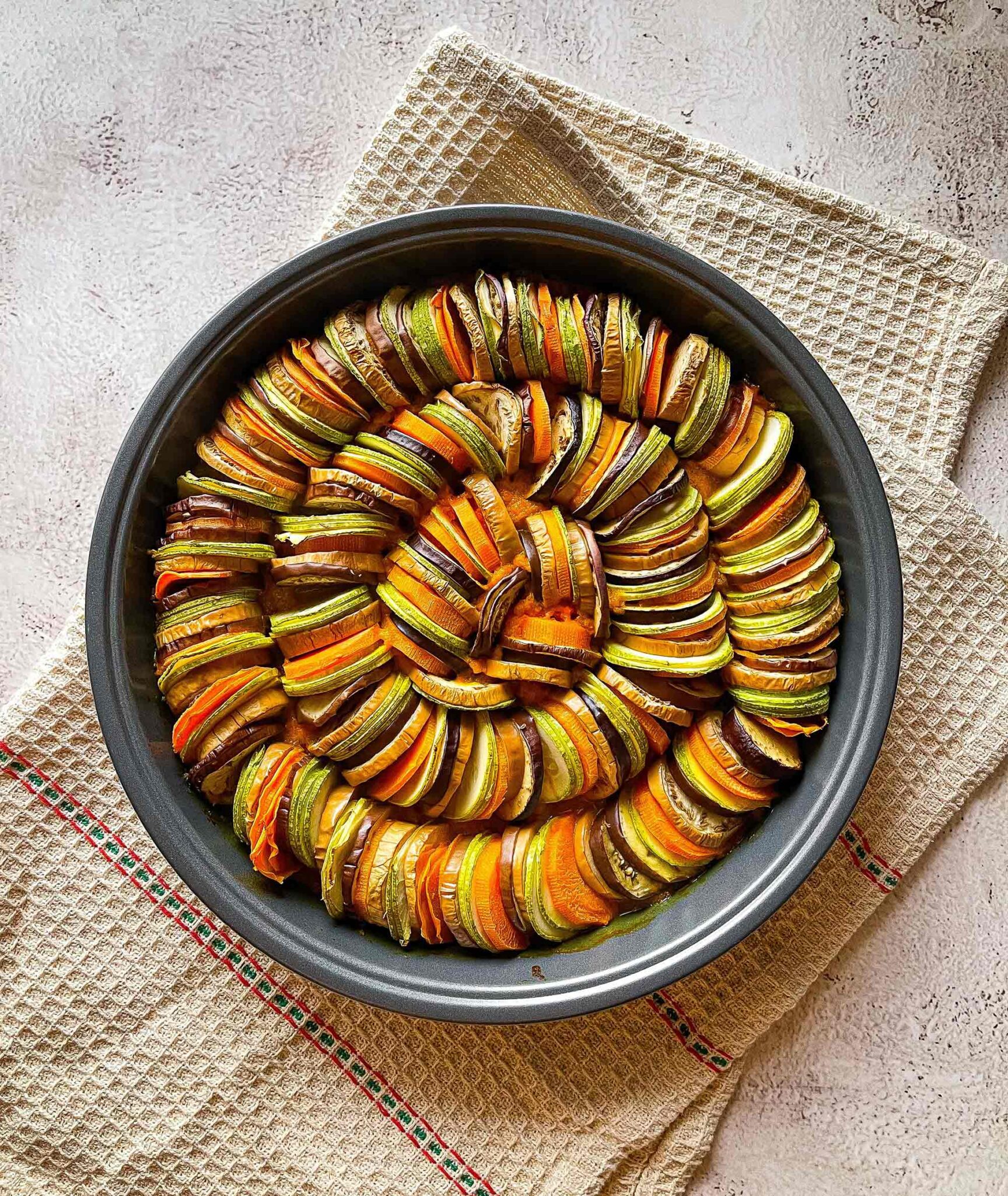 Spiralförmig angerichtetes Ratatouille aus Zucchini, Aubergine, Paprika und Tomaten in der Auflaufform