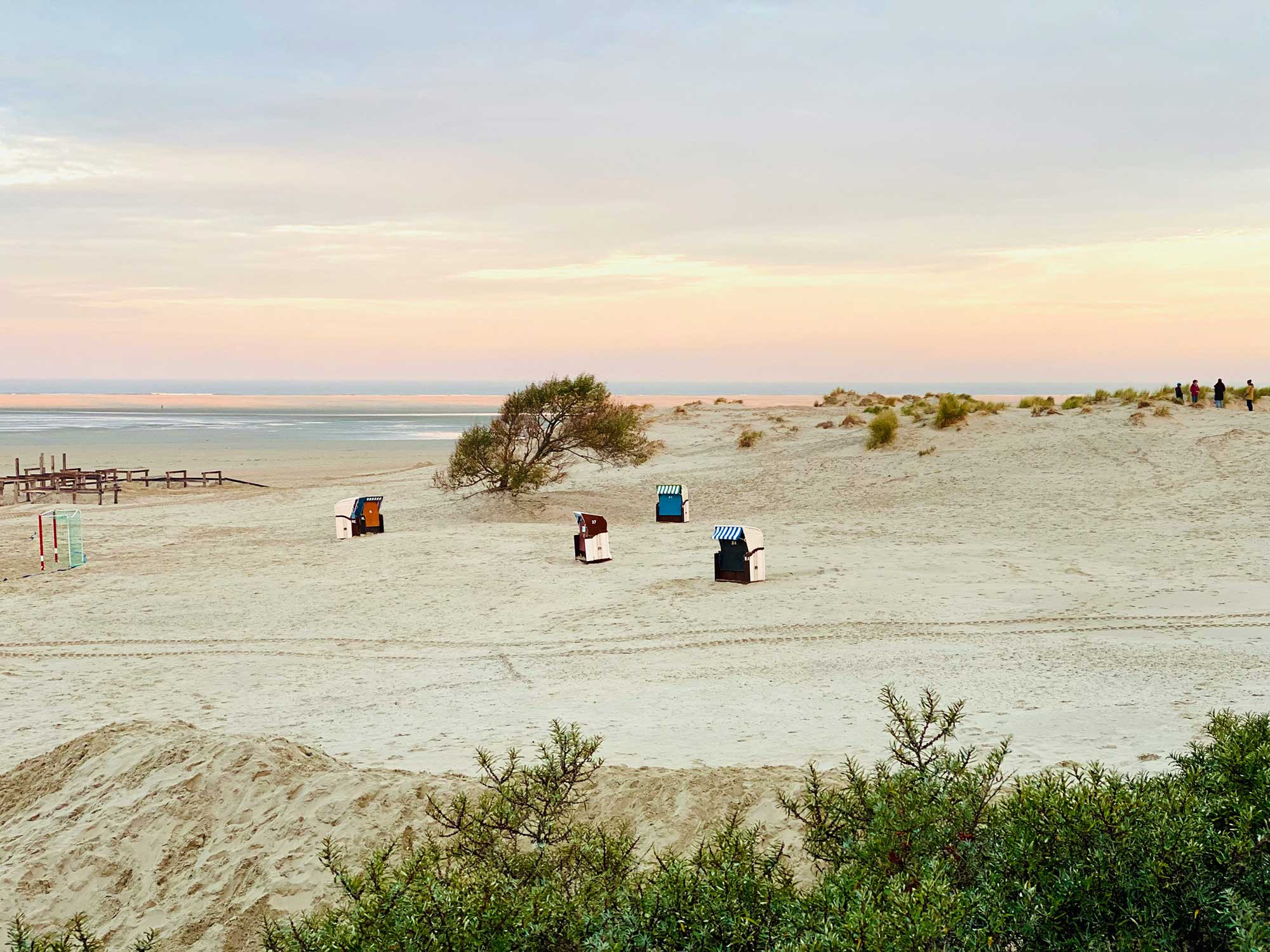 Wattenmeer an der Nordseeküste bei Sonnenuntergang mit Strandkörben in den Dünen