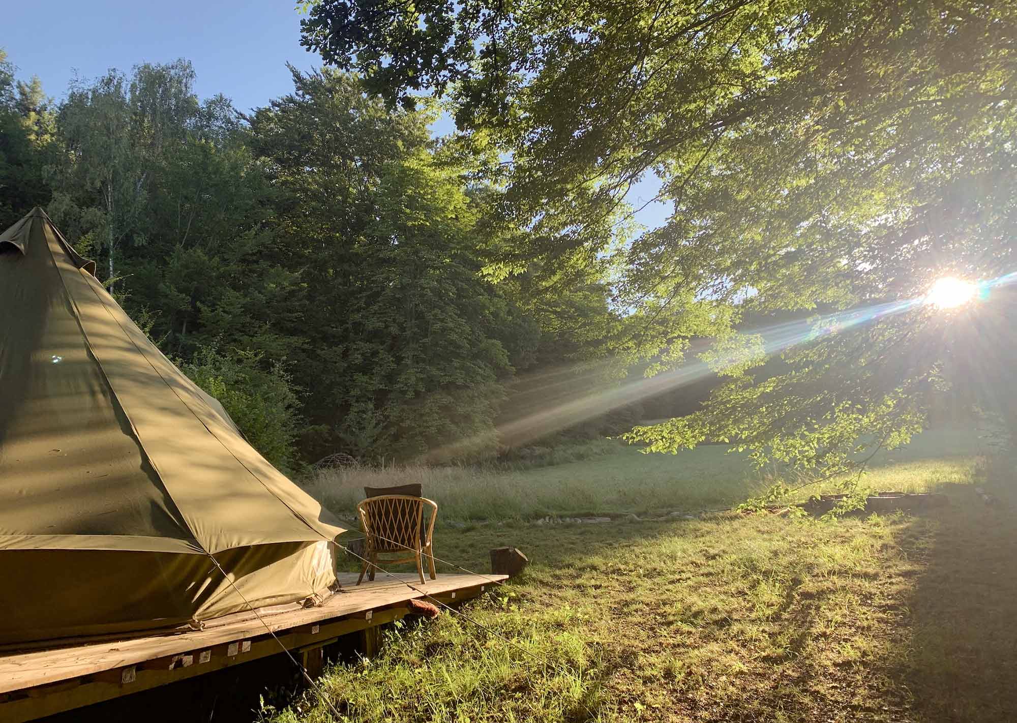 Rundzelt auf Holzplattform mit Stuhl und Blick auf Wiese und Wald bei Sonnenaufgang, Mucherwiese