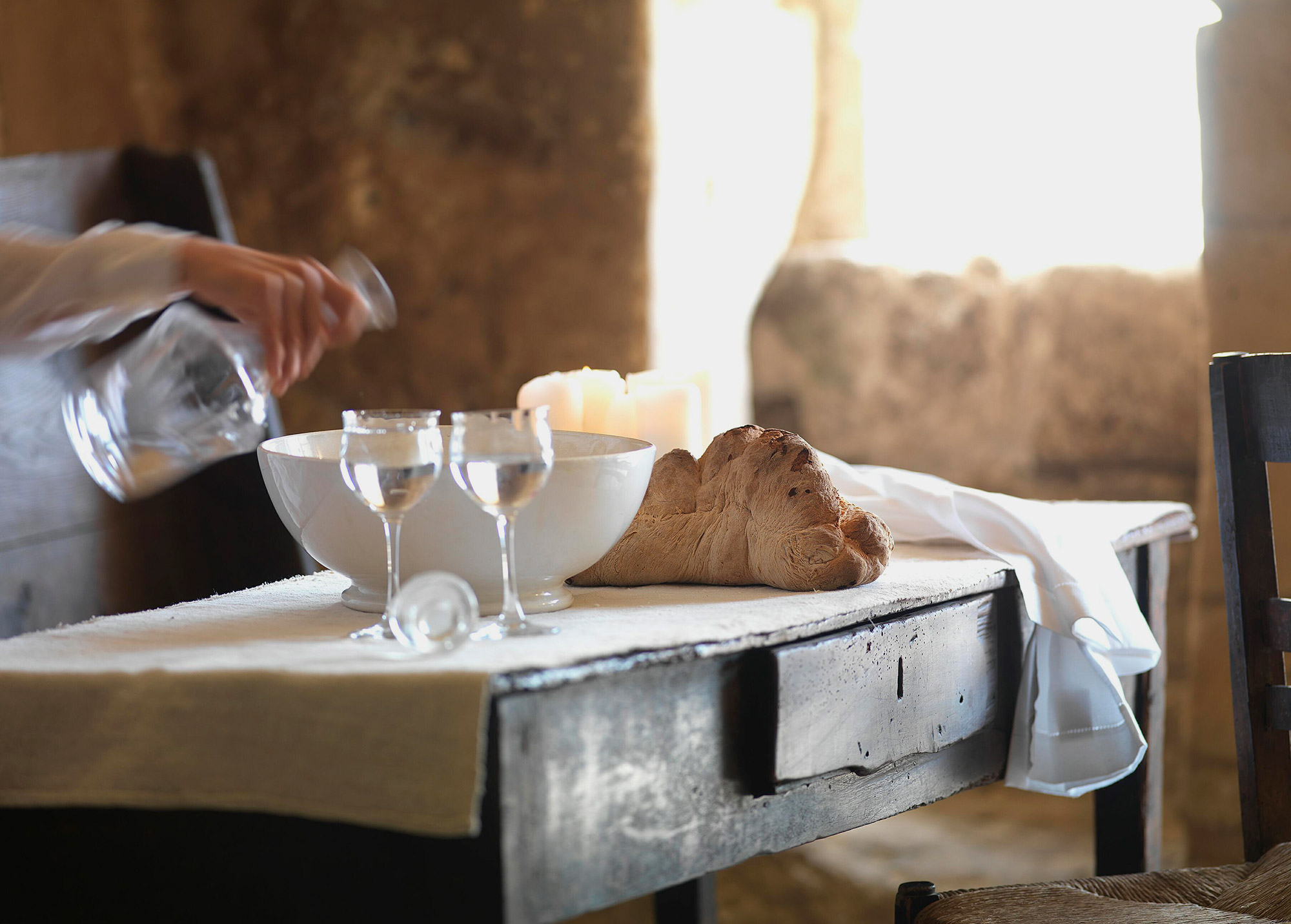 Tisch mit frischem Brot, Weingläsern und Kerzenlicht wird für ein Abendessen gedeckt