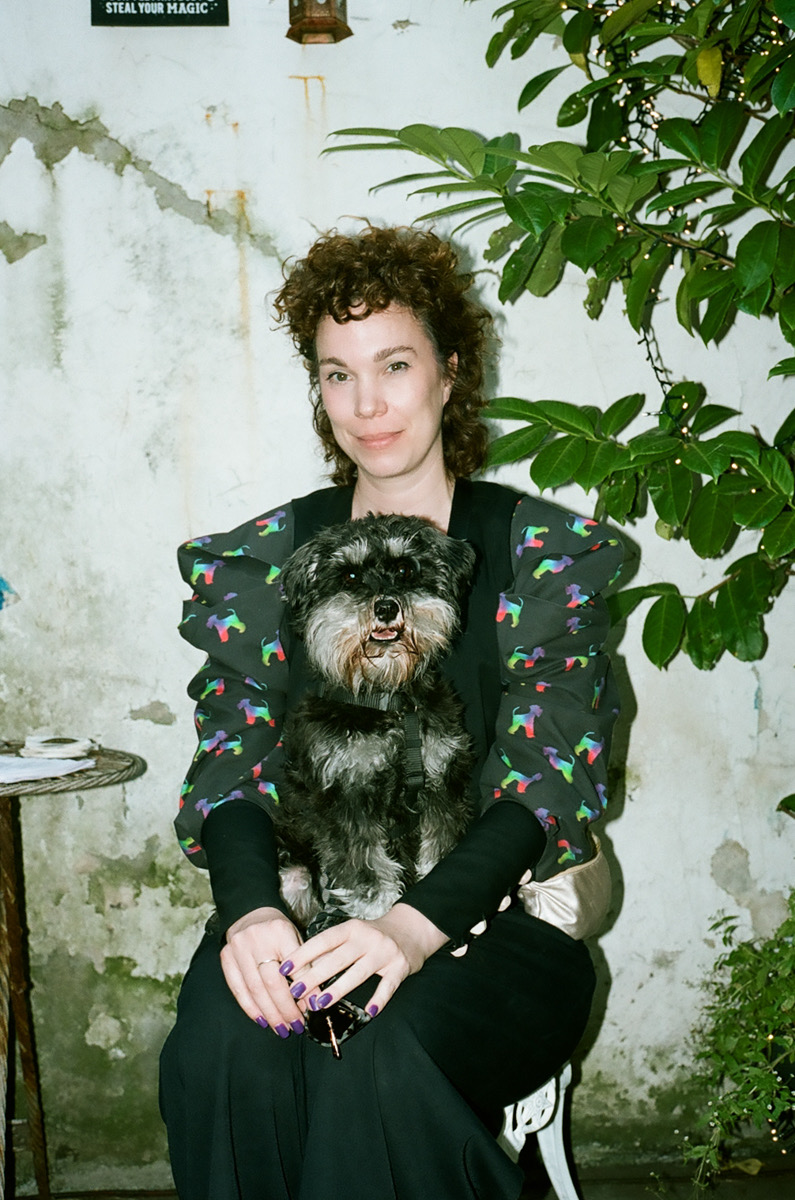 Modedesignerin Angelika Kauffmann sitzt lächelnd mit ihrem Hund Otte auf dem Schoß, sie trägt einen bunt gemusterten Blazer mit Puffärmeln