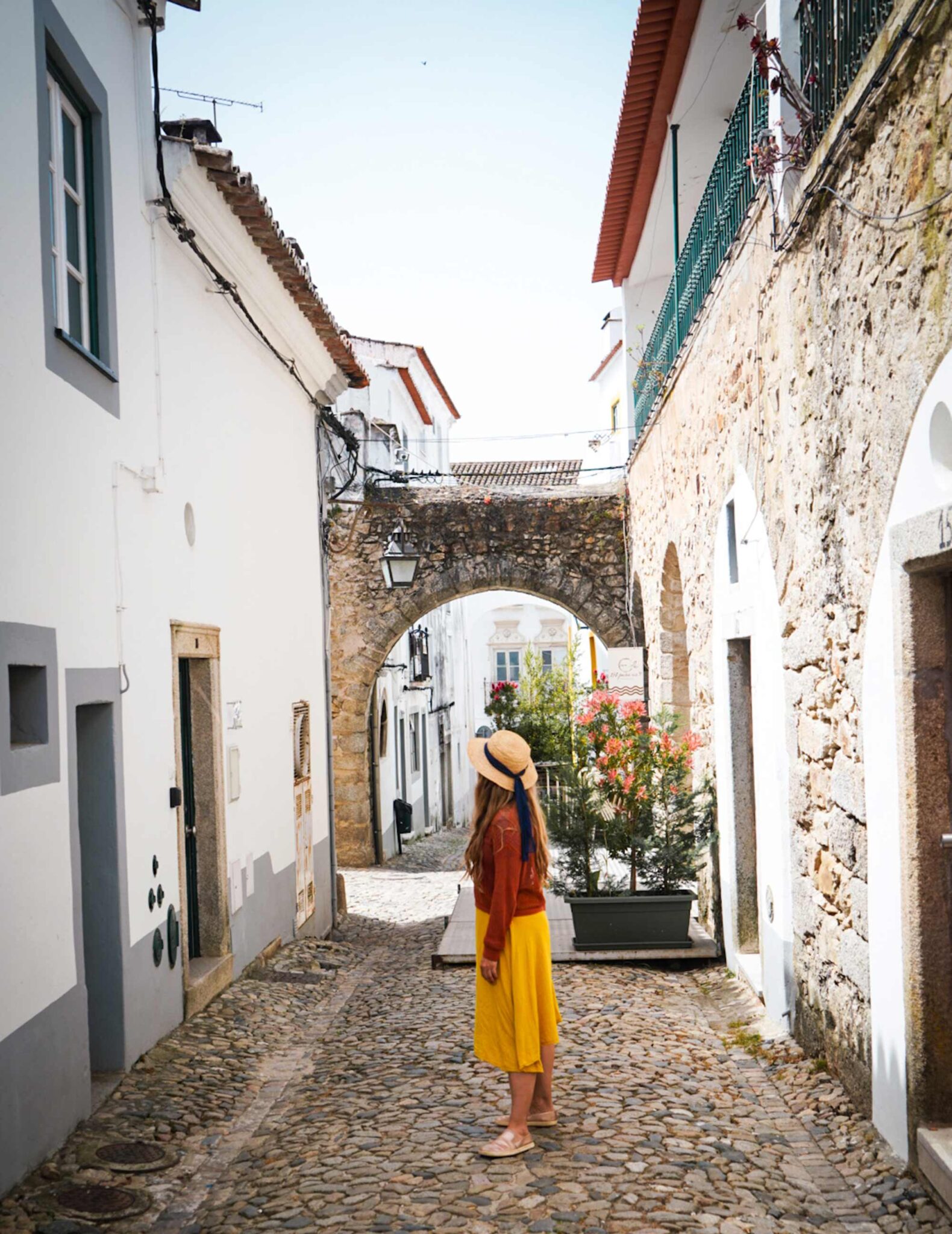 Frau im gelben Rock geht durch eine enge Gasse mit historischem Steinbogen in der Altstadt von Évora