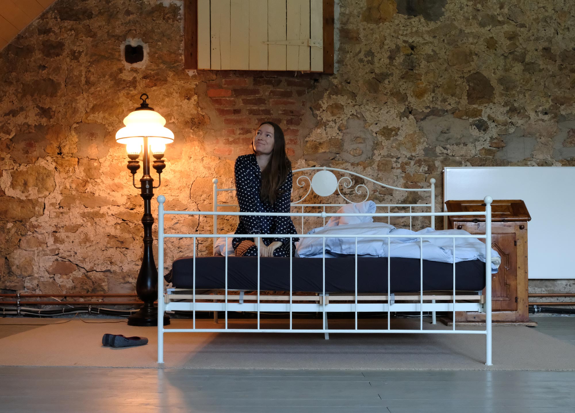 Rustikales Schlafzimmer im Verwalterhaus von Gut Neuwerk mit Natursteinwand, Vintage-Stehlampe und weißem Metallbett