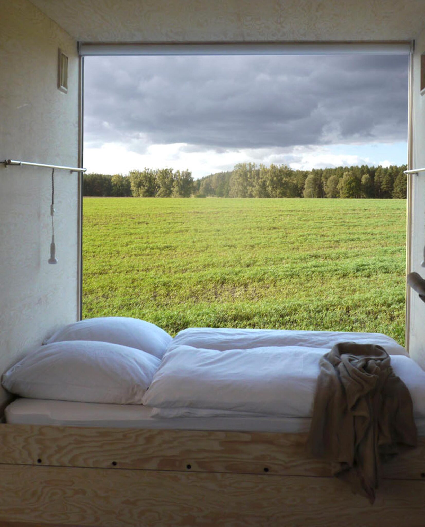 Bett vor großem Fenster mit Blick auf Wiese und Wald im Zimmer Salix des Re:hof Rutenberg