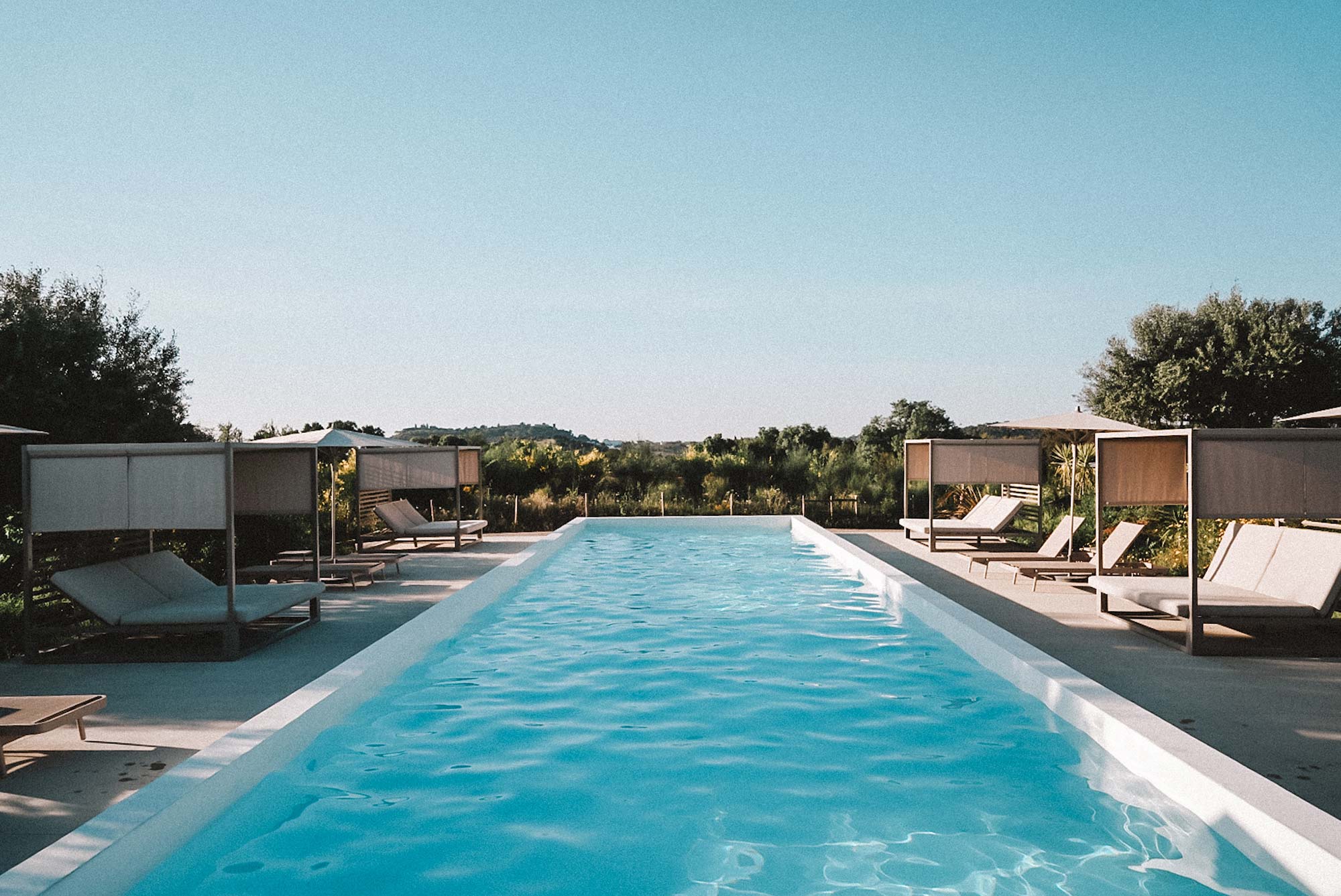 Infinity-Pool des Gandum Village mit Loungebetten und Blick auf die Landschaft des Alentejo