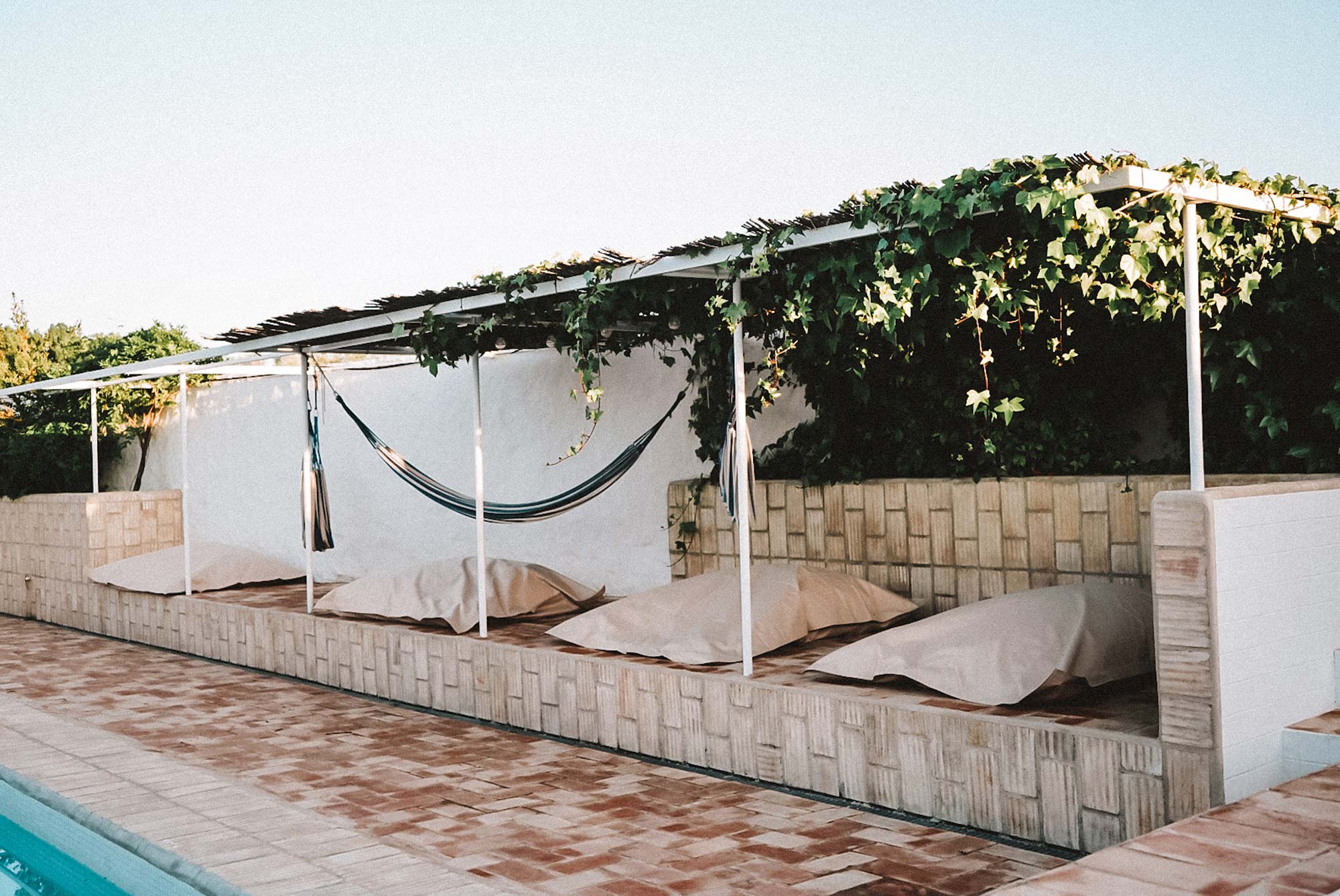 Gemütlicher Loungebereich mit Sitzkissen und Hängematte unter einer Pergola am Pool des Gandum Village