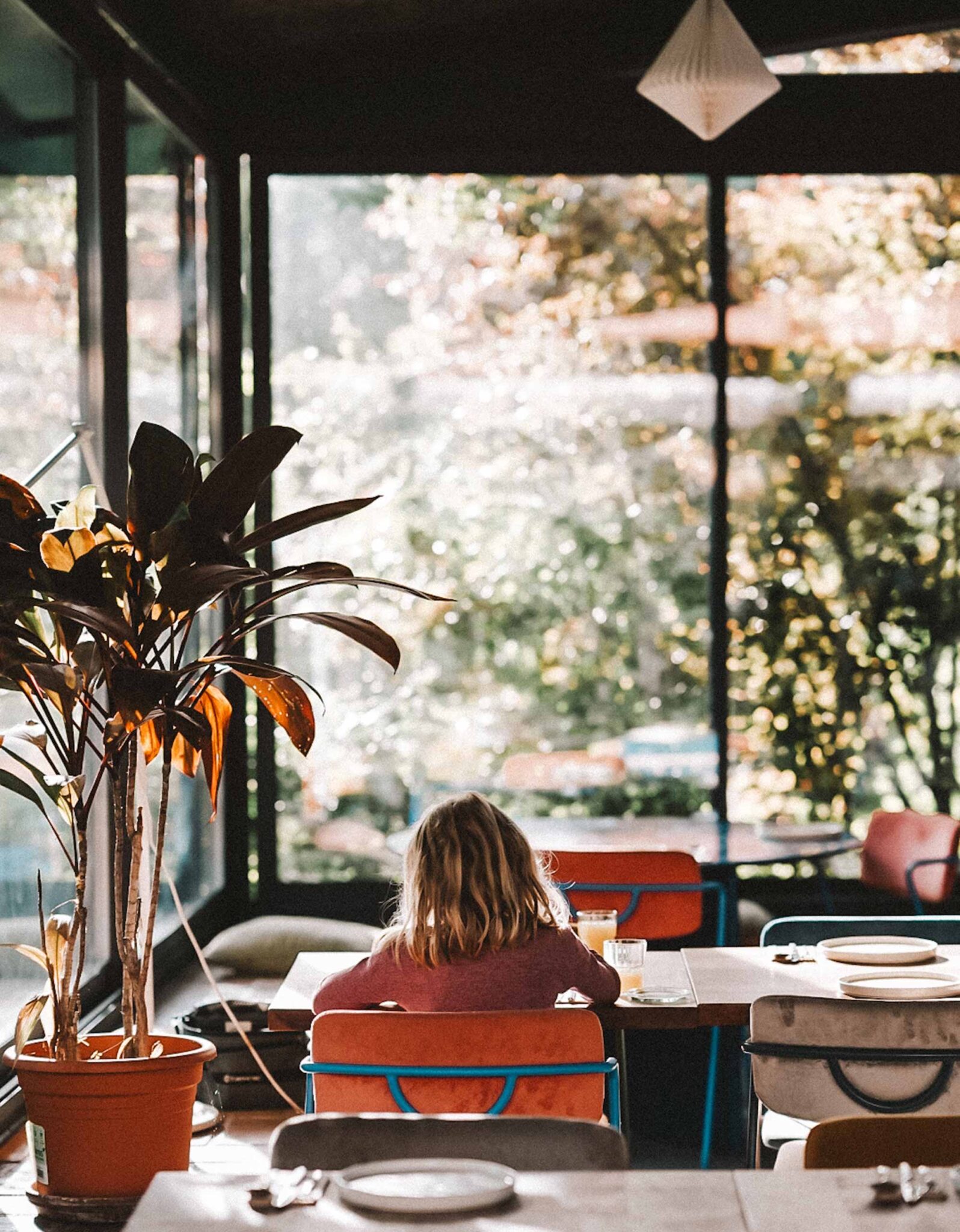 Mädchen sitzt am Fenstertisch im Restaurant Provenance des Gandum Village mit Blick ins Grüne