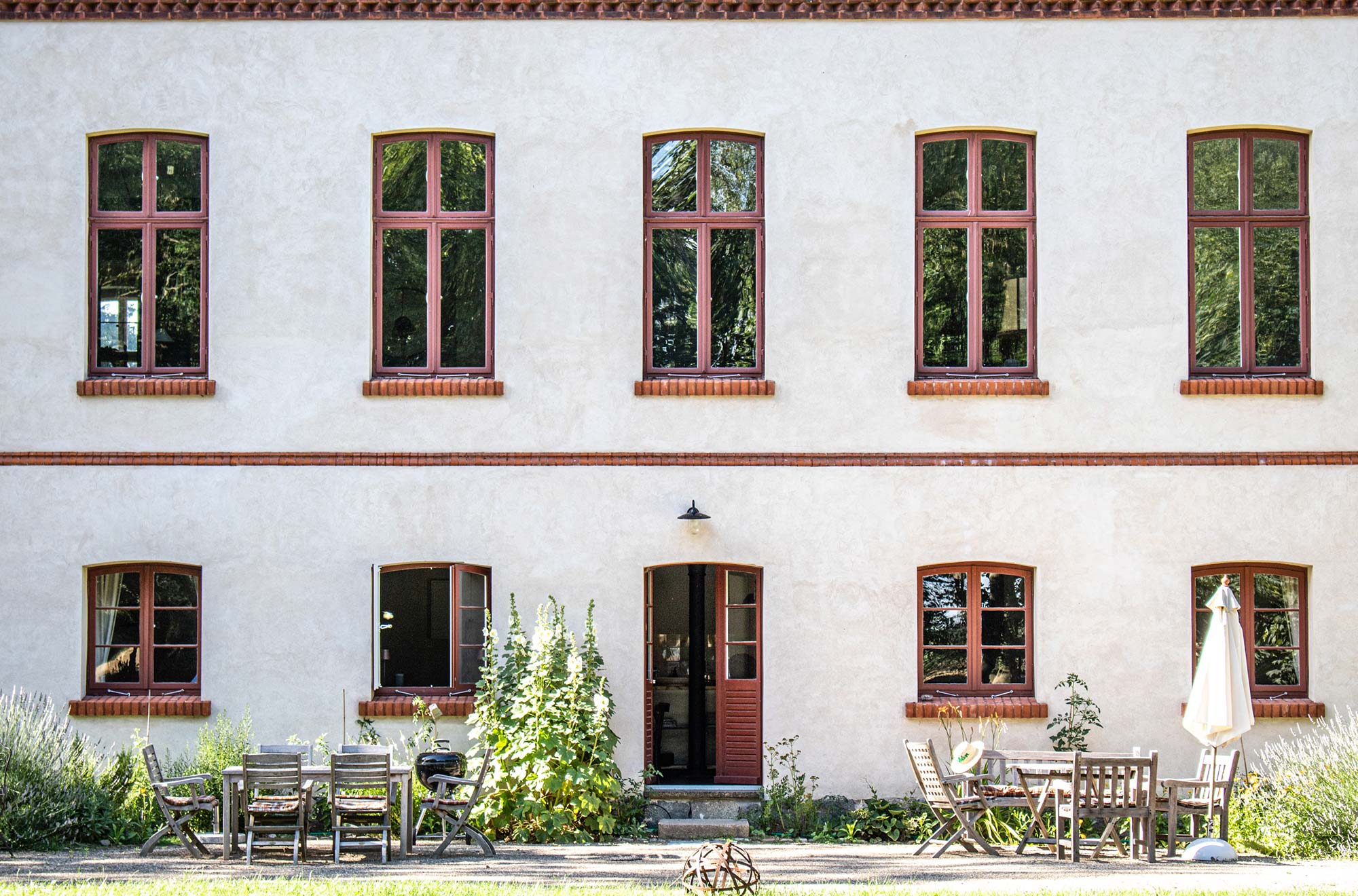 Historische Fassade des Gutshauses Zarchlin mit roten Fensterrahmen und Gartenterrasse